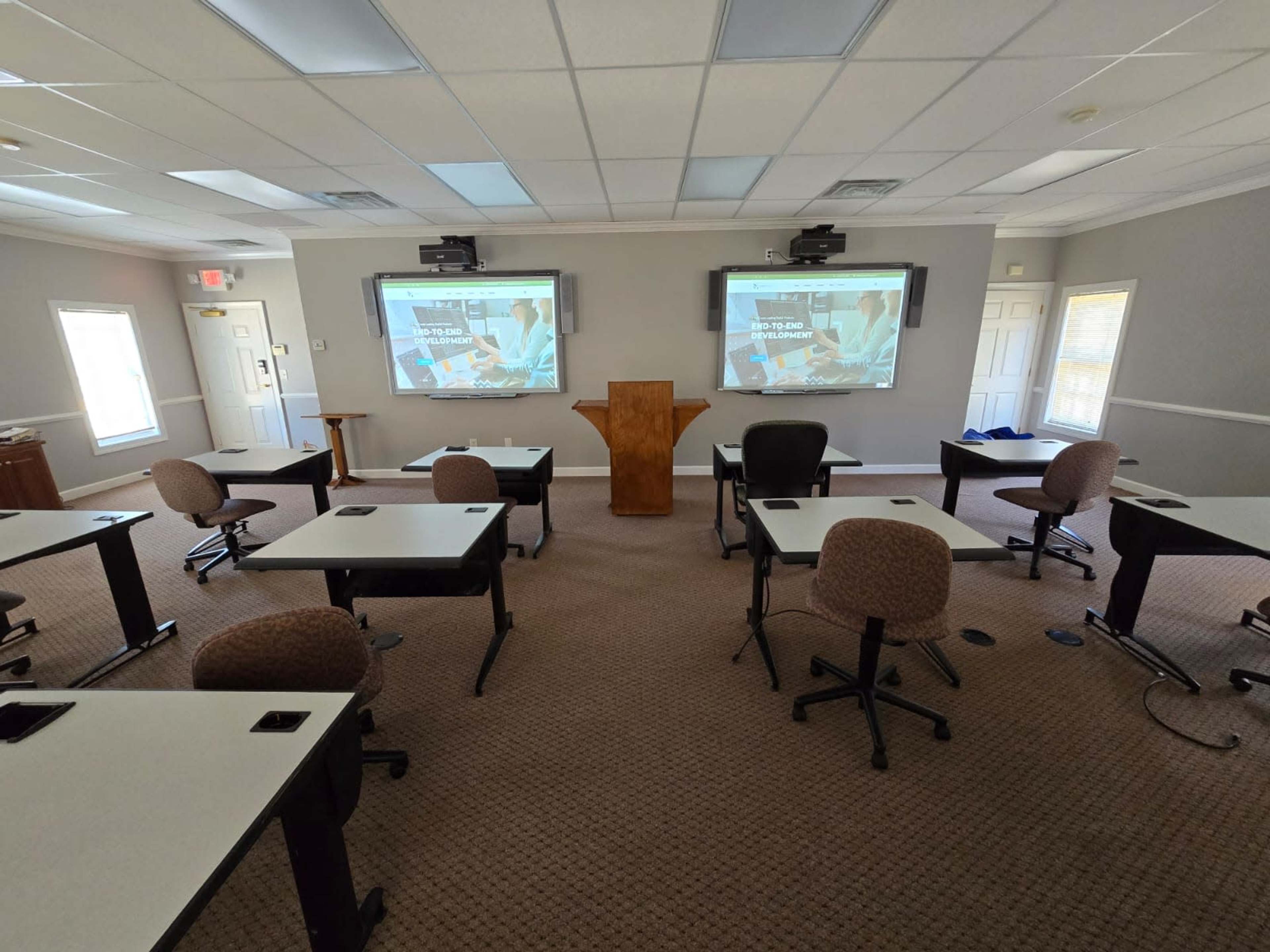 A classroom setup with multiple desks and two projection screens displaying a presentation.