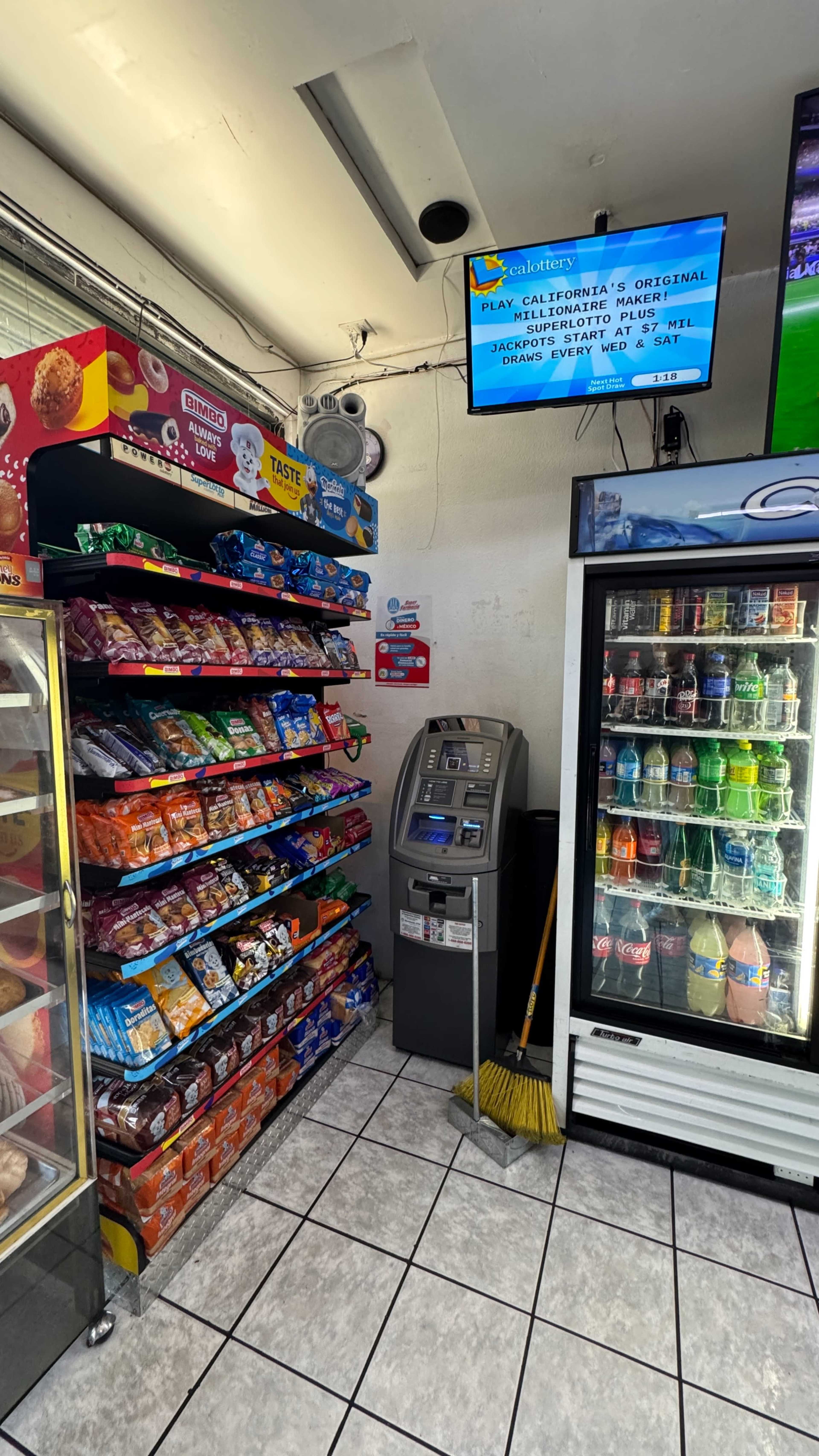 The image shows an interior of a convenience store with shelves filled with snacks, a beverage cooler, an ATM, and a television displaying a sports game.