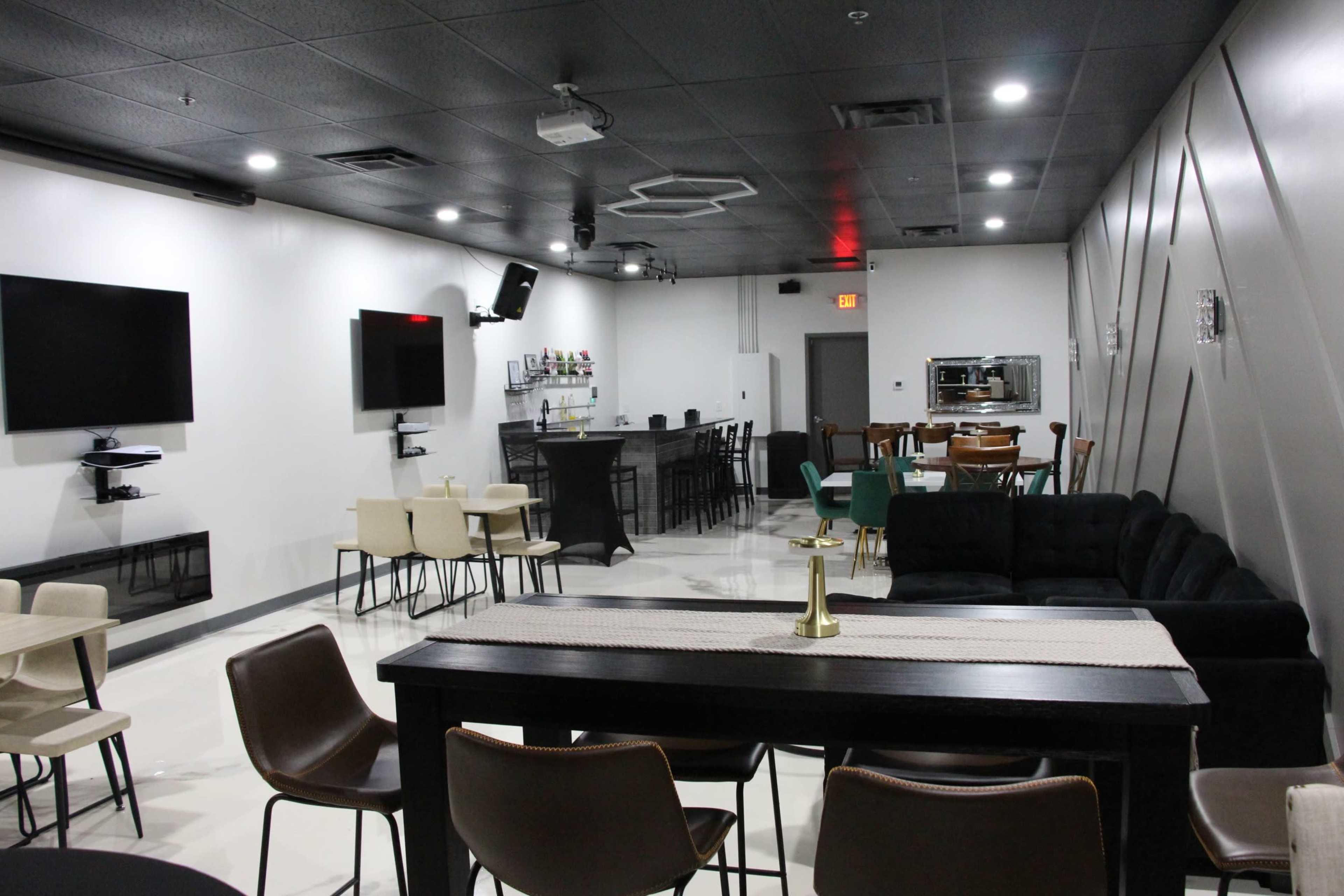 A modern lounge space featuring a bar area, multiple seating arrangements, and wall-mounted televisions.