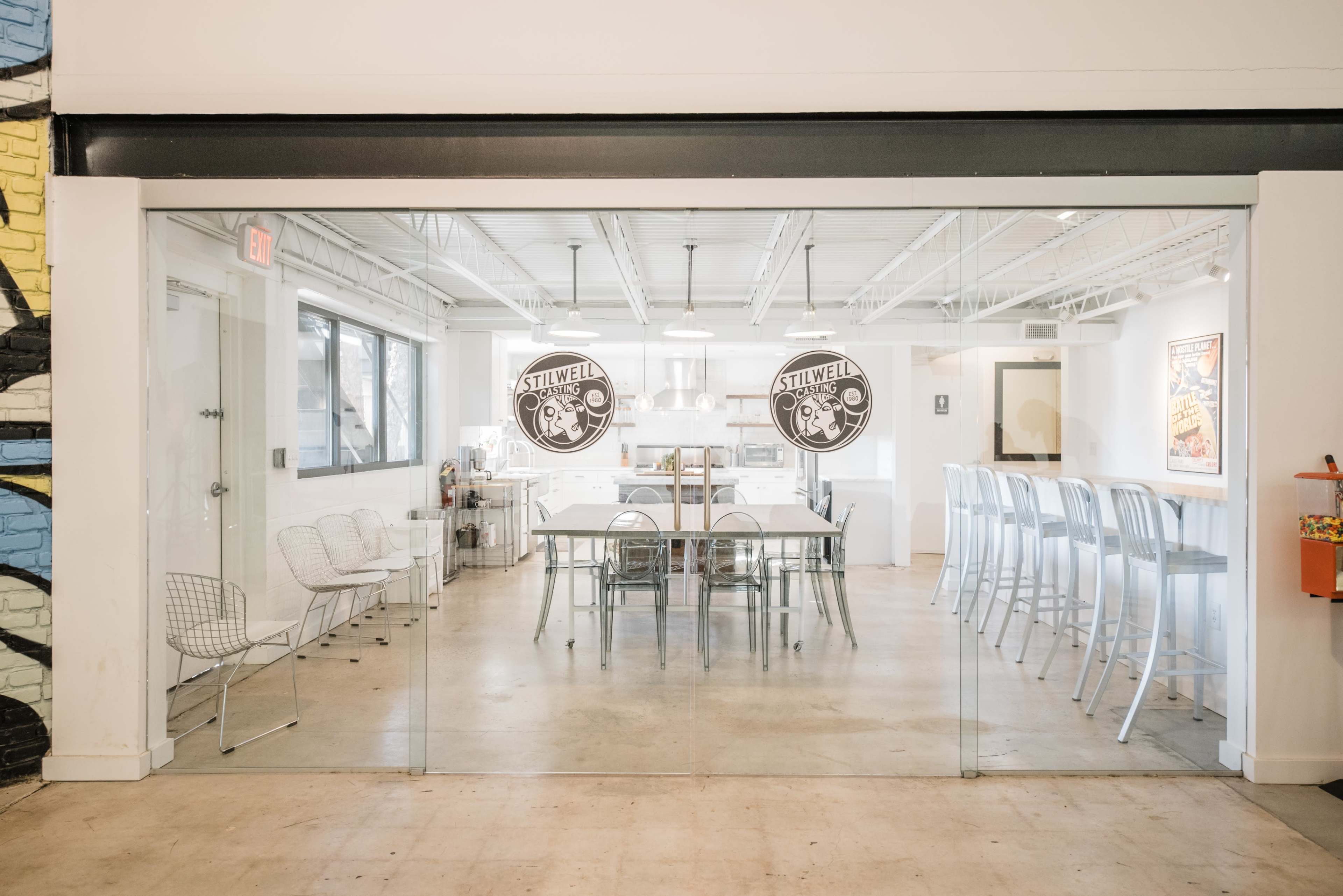 A modern, open dining area with a glass wall, featuring a large table, bar seating, and stainless steel appliances in a well-lit space.
