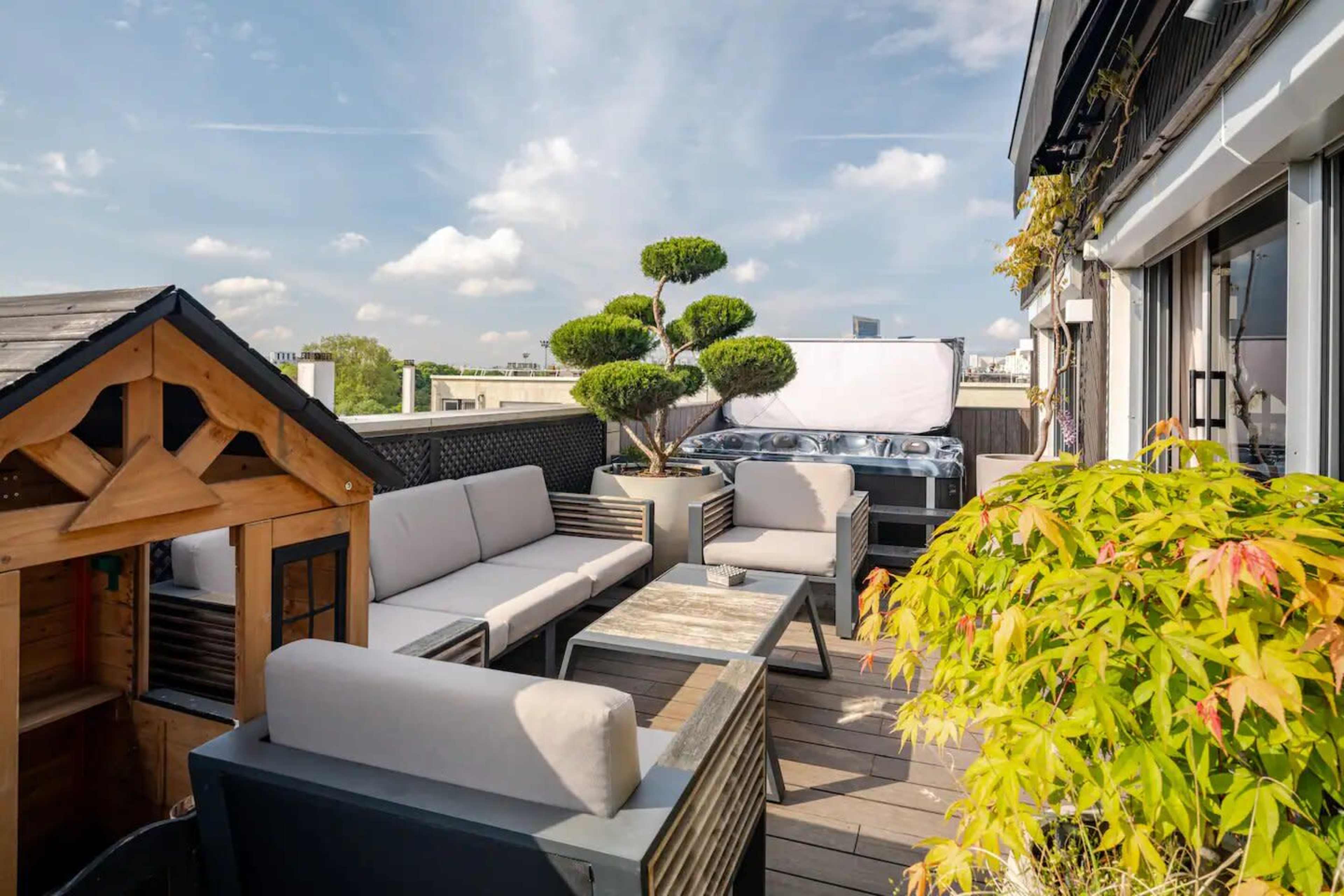 The rooftop terrace features modern seating, a hot tub, and a bonsai tree surrounded by greenery.