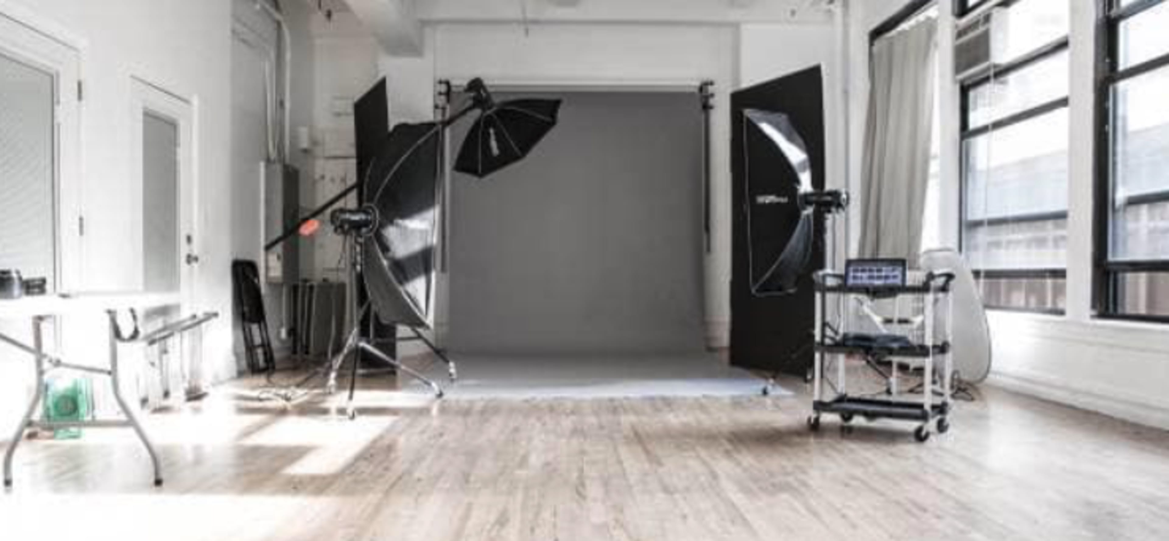 The image shows a photography studio equipped with lighting equipment, a backdrop, and preparation areas.