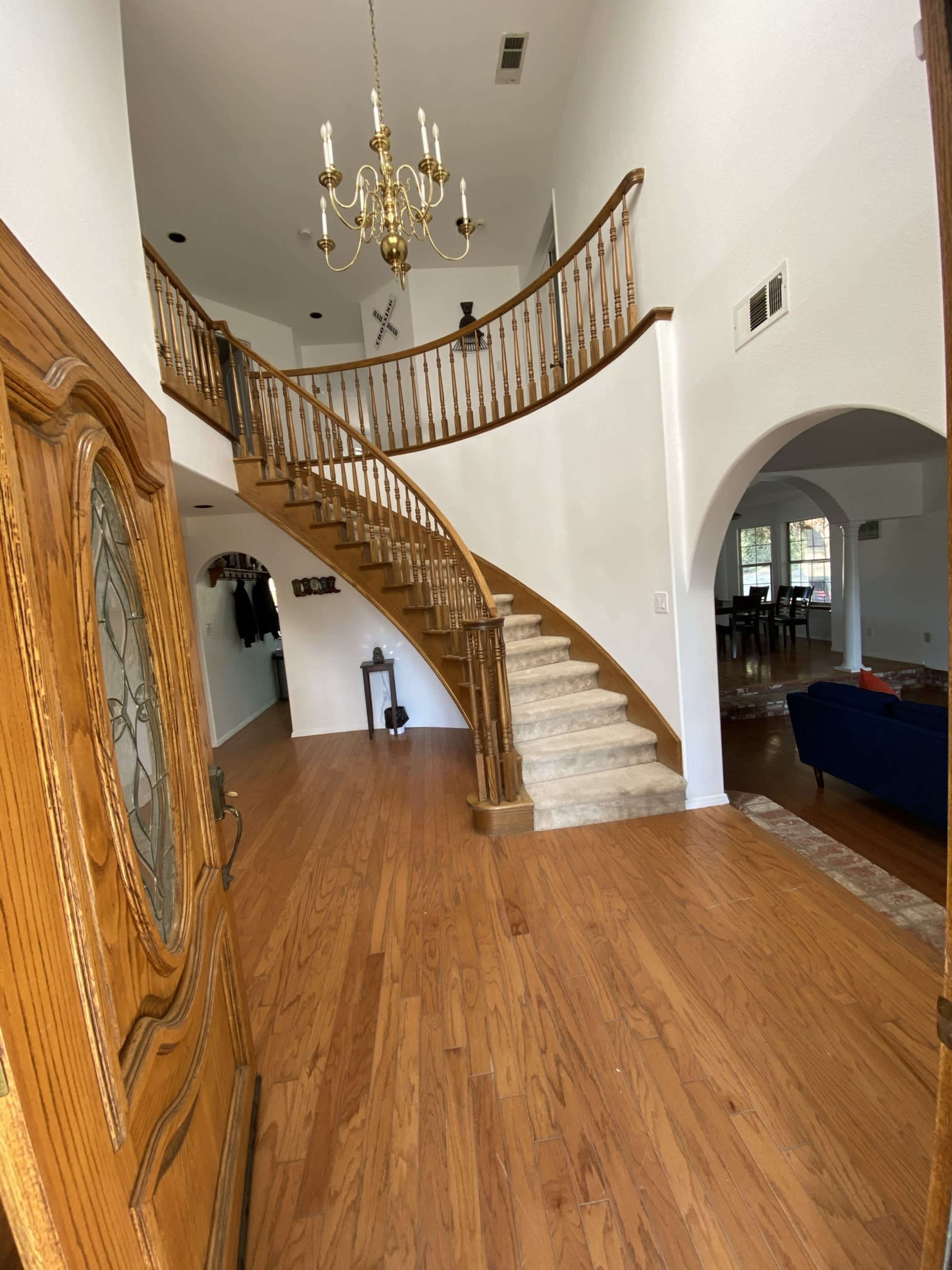 A spacious foyer with a wooden staircase, chandelier, and hardwood flooring leading to an open dining area.