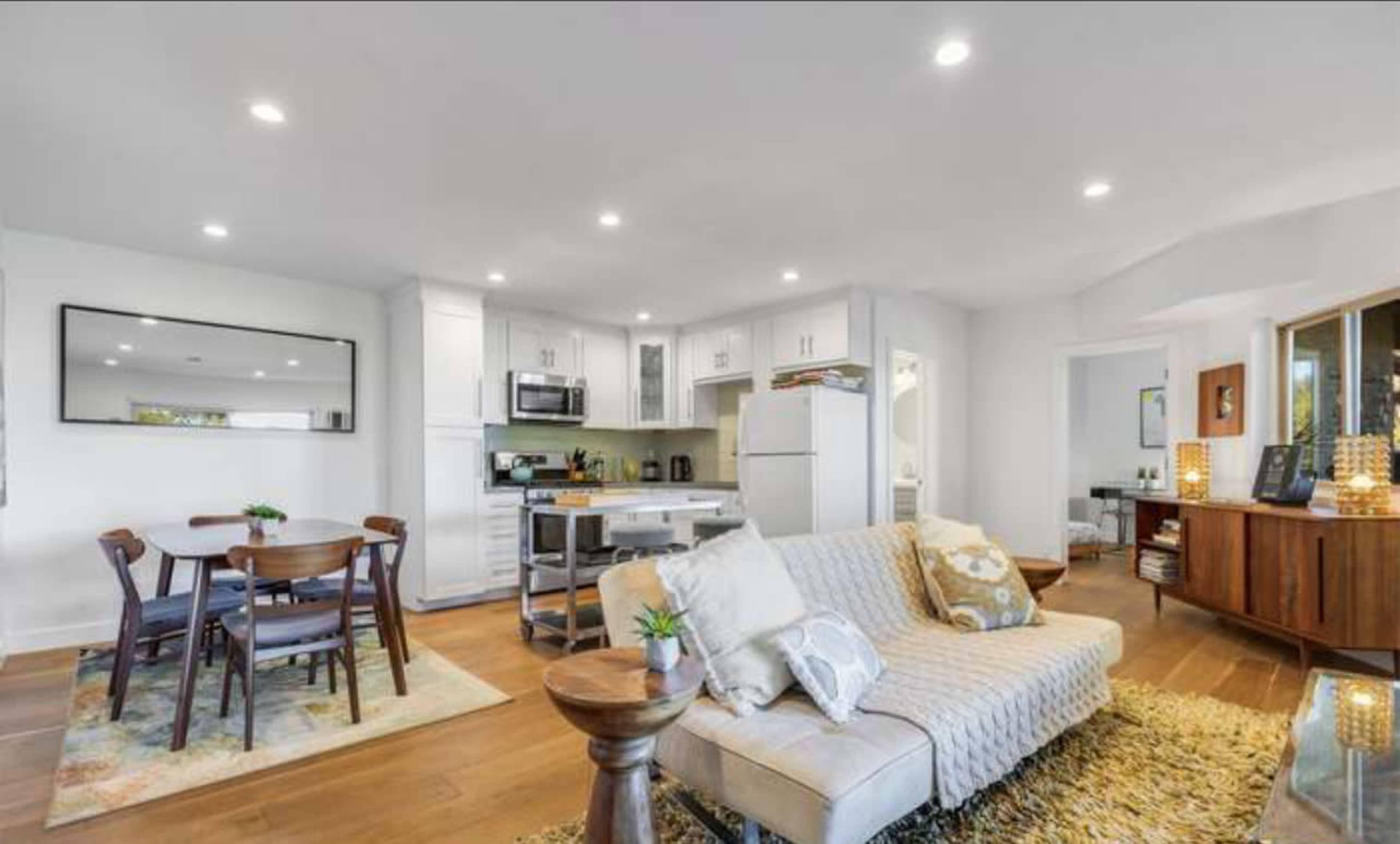 The image shows a modern open-concept living space featuring a kitchen, dining area with a round table, and a cozy seating arrangement.