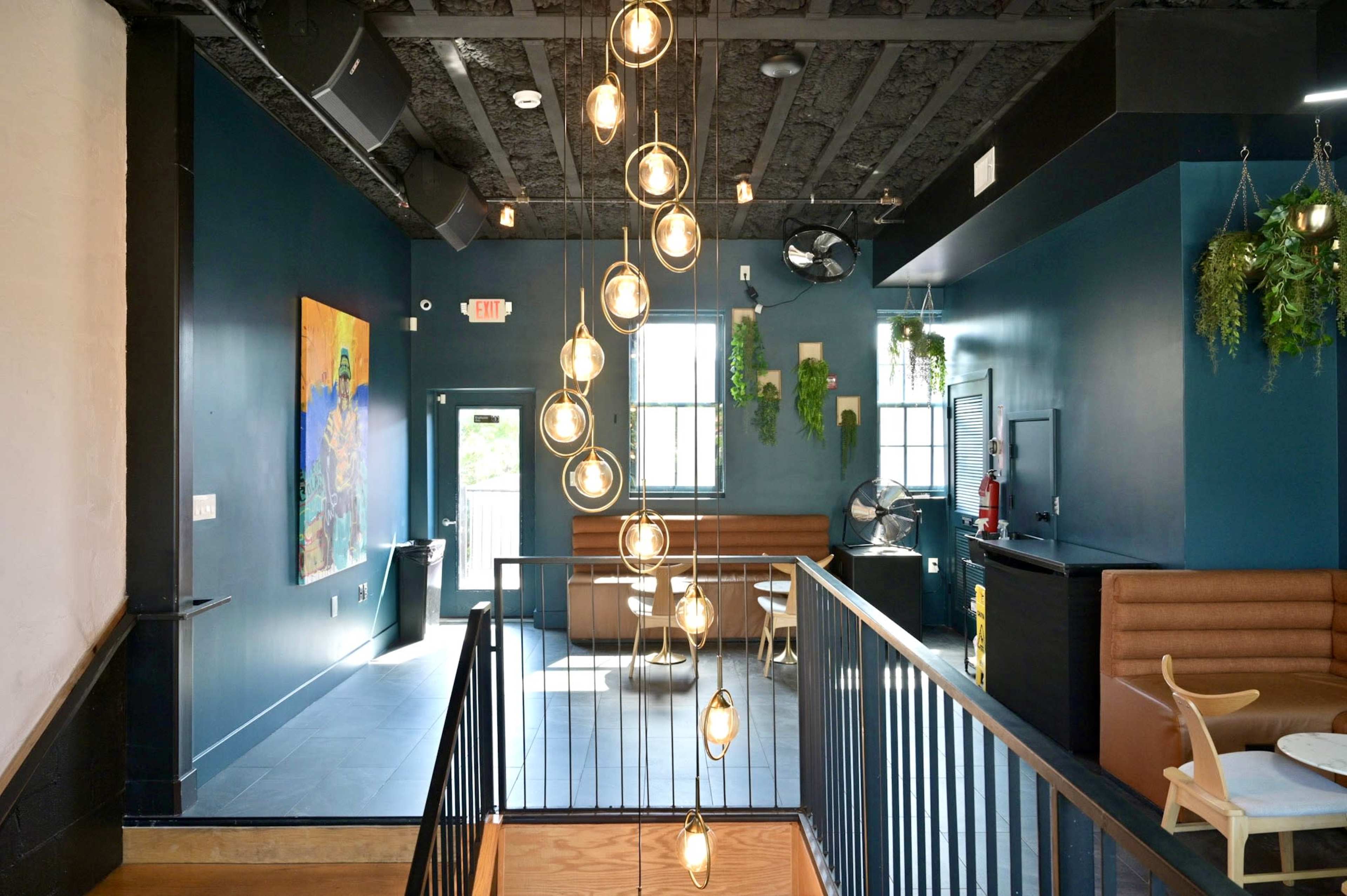 The image shows a modern interior space featuring dark blue walls, pendant lighting, and a staircase leading to a seating area.