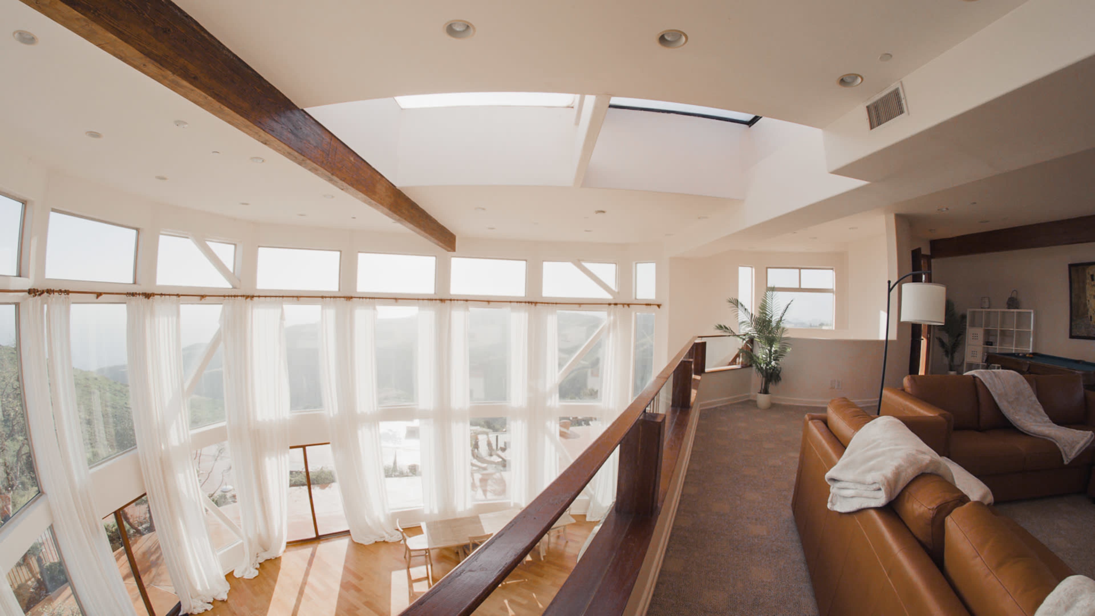 A spacious interior features large windows, wooden beams, and a blend of cozy seating and dining furniture.