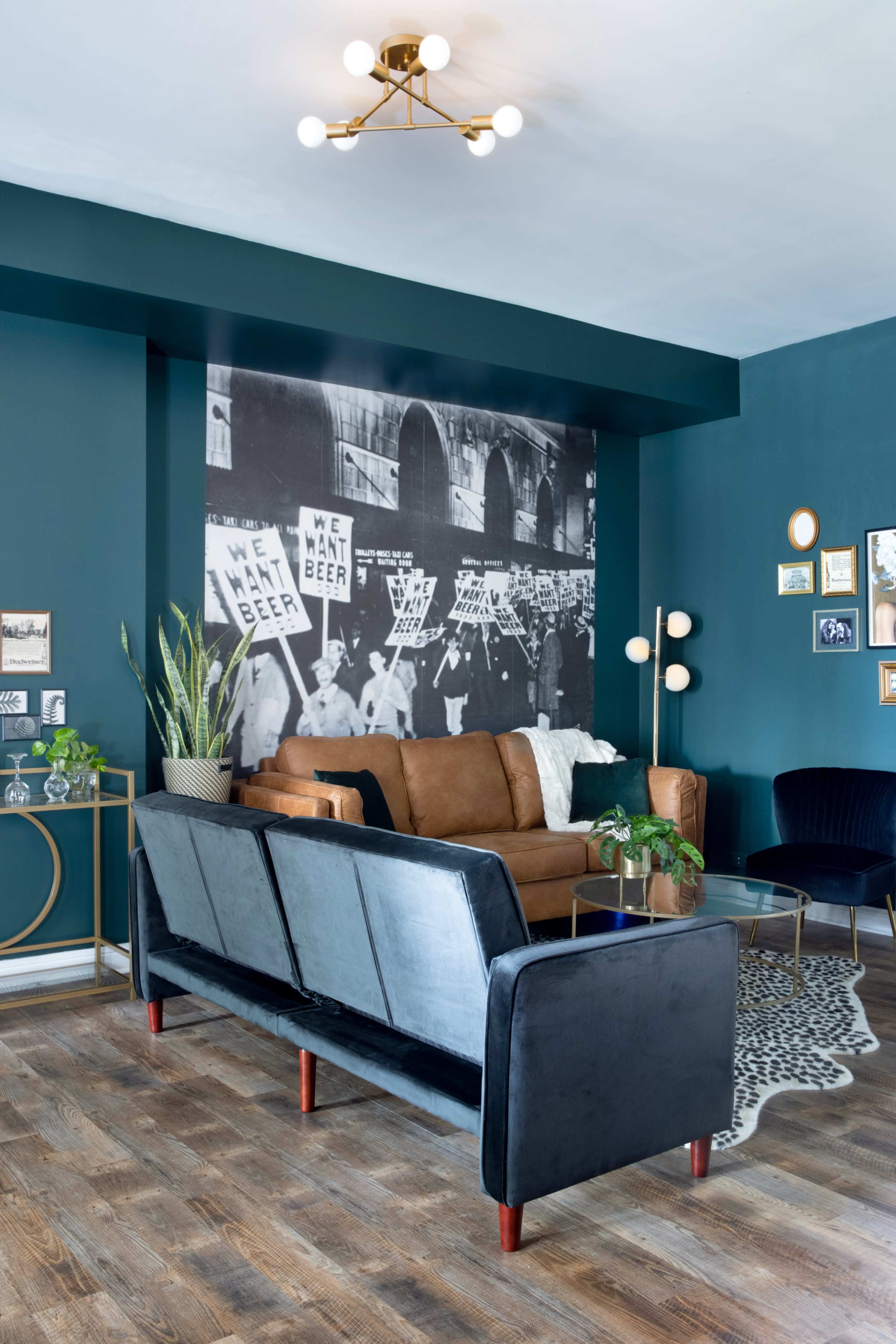 The image depicts a stylish living room with a dark teal accent wall featuring a large black-and-white mural, a brown leather sofa, and a modern light fixture.
