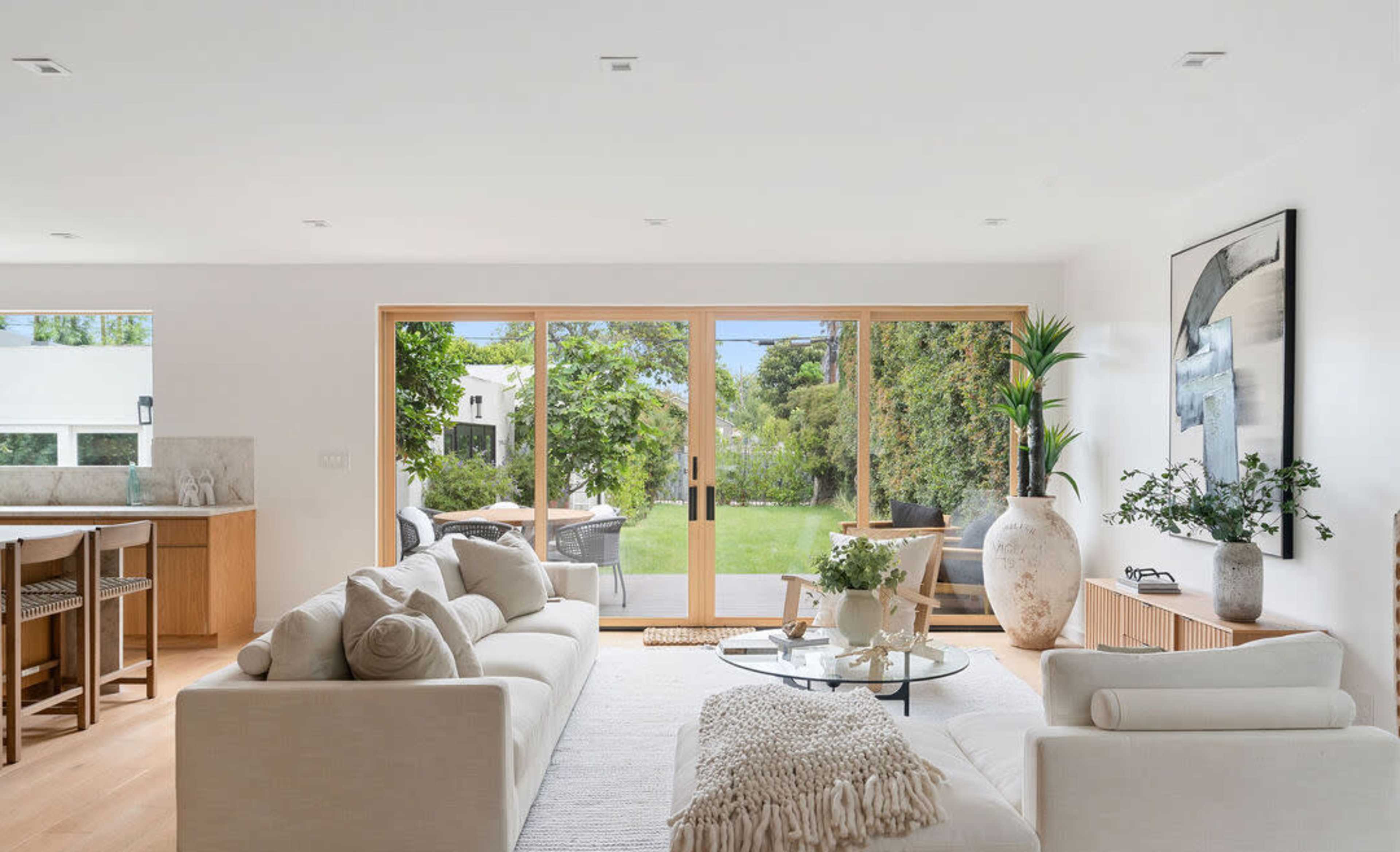 A modern living room features a cream sofa and glass coffee table, with large sliding doors opening to a green backyard.