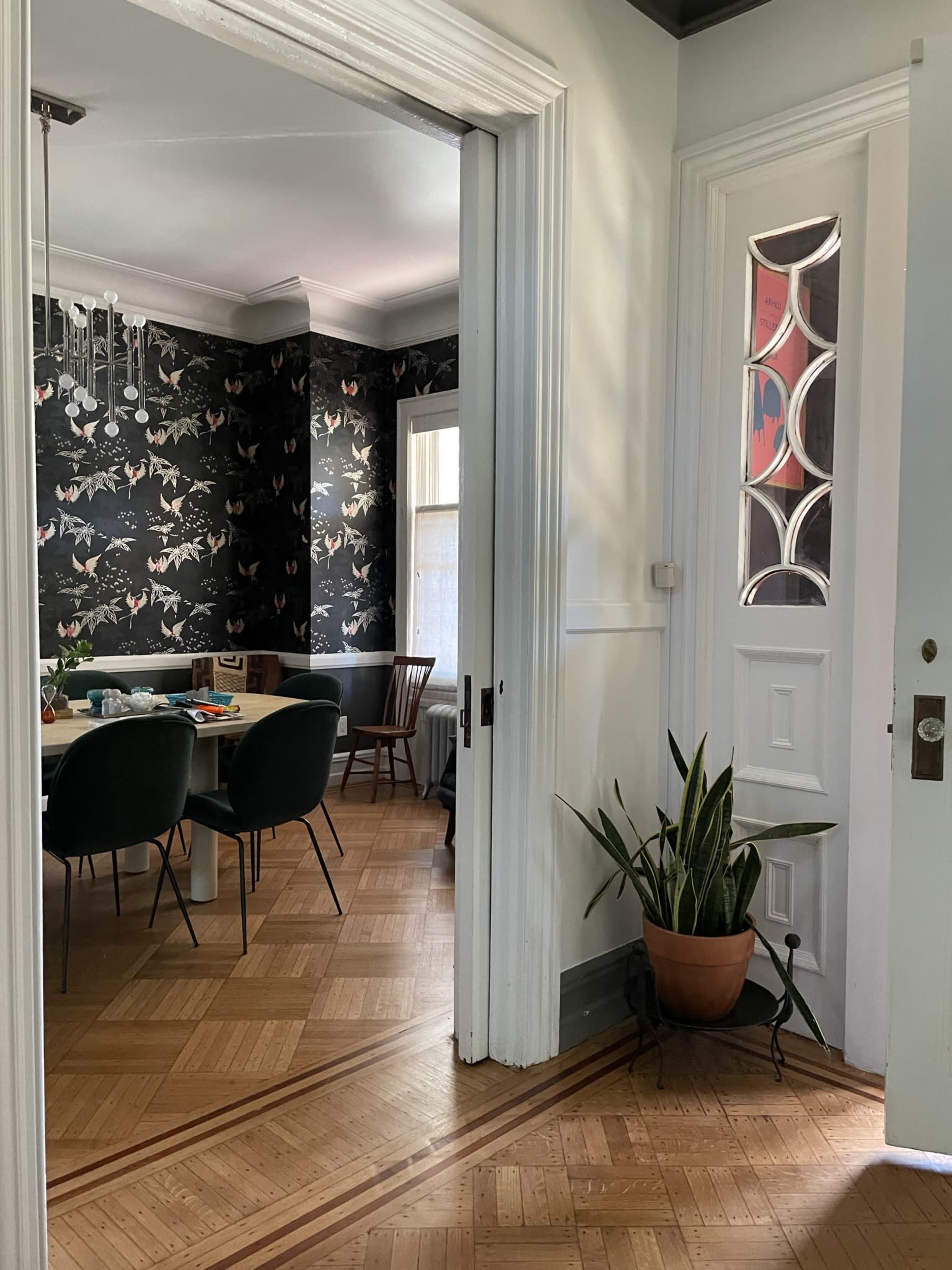 A view through an open doorway shows a dining area with a dark floral wallpaper, a table set for a meal, and a potted plant near the entrance.