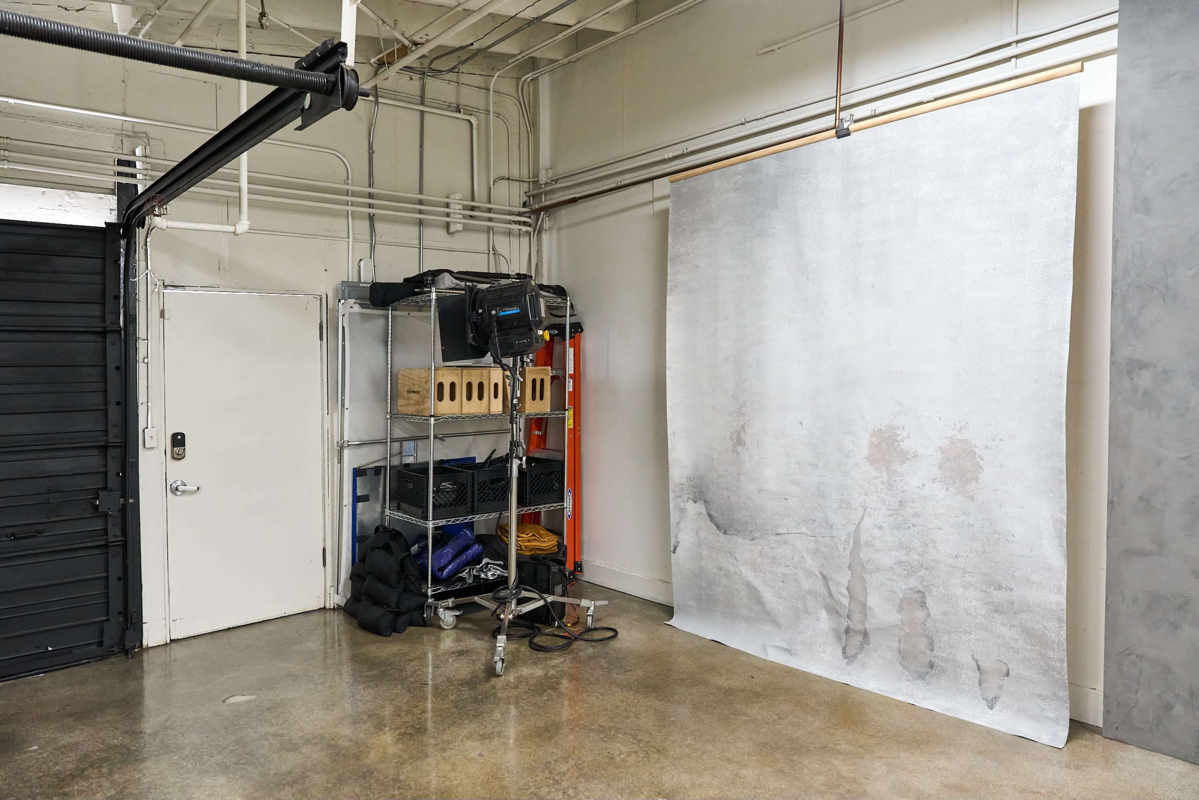 A corner of a room featuring a shelving unit with equipment and a large, rolled backdrop against the wall.