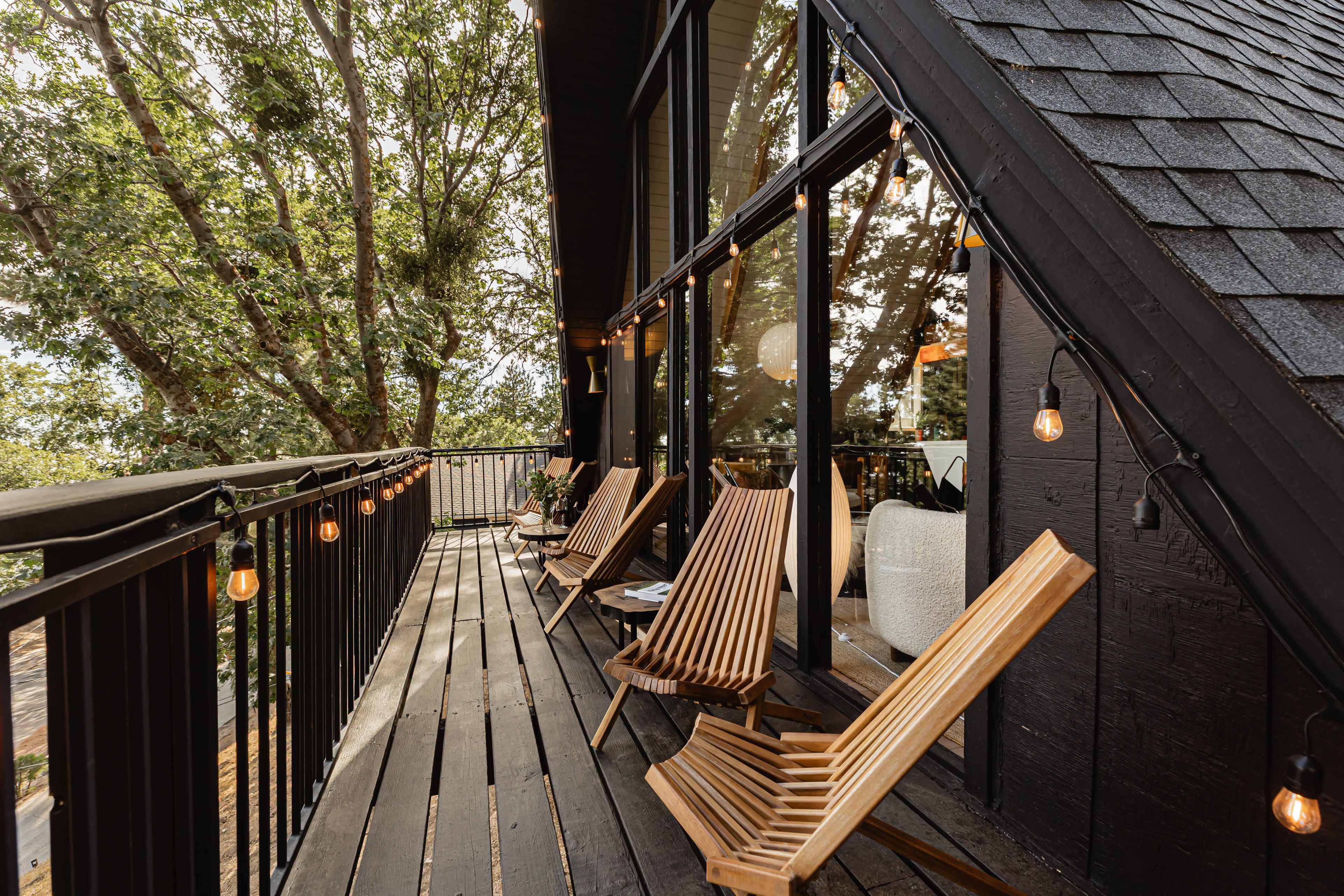 A balcony features wooden lounge chairs lined along the railing, with greenery visible in the background.