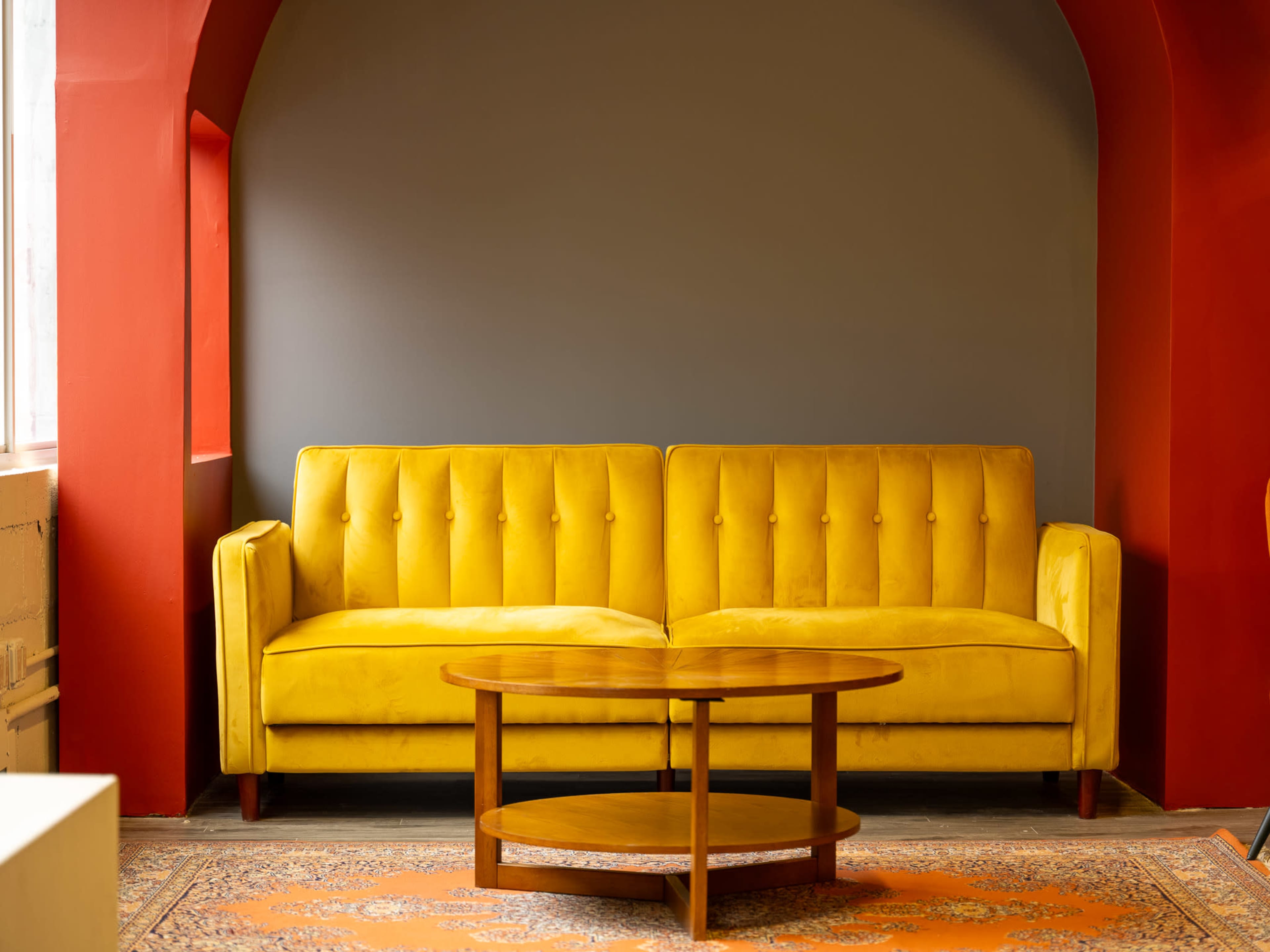A yellow tufted sofa is positioned against a gray wall, with a round wooden coffee table in front of it.