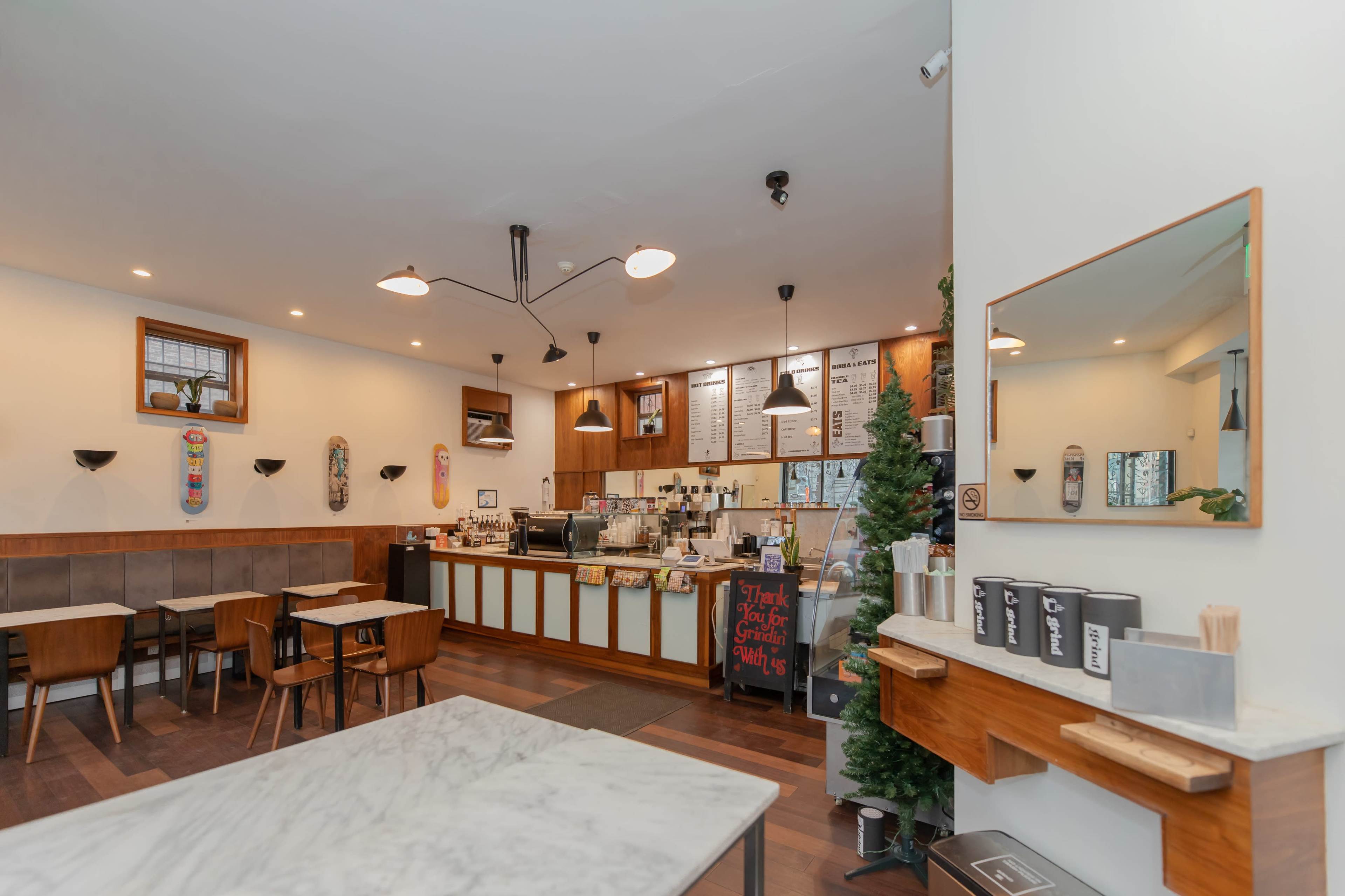 A cozy café interior with wooden tables, a counter displaying menu items, and a festive decoration in one corner.