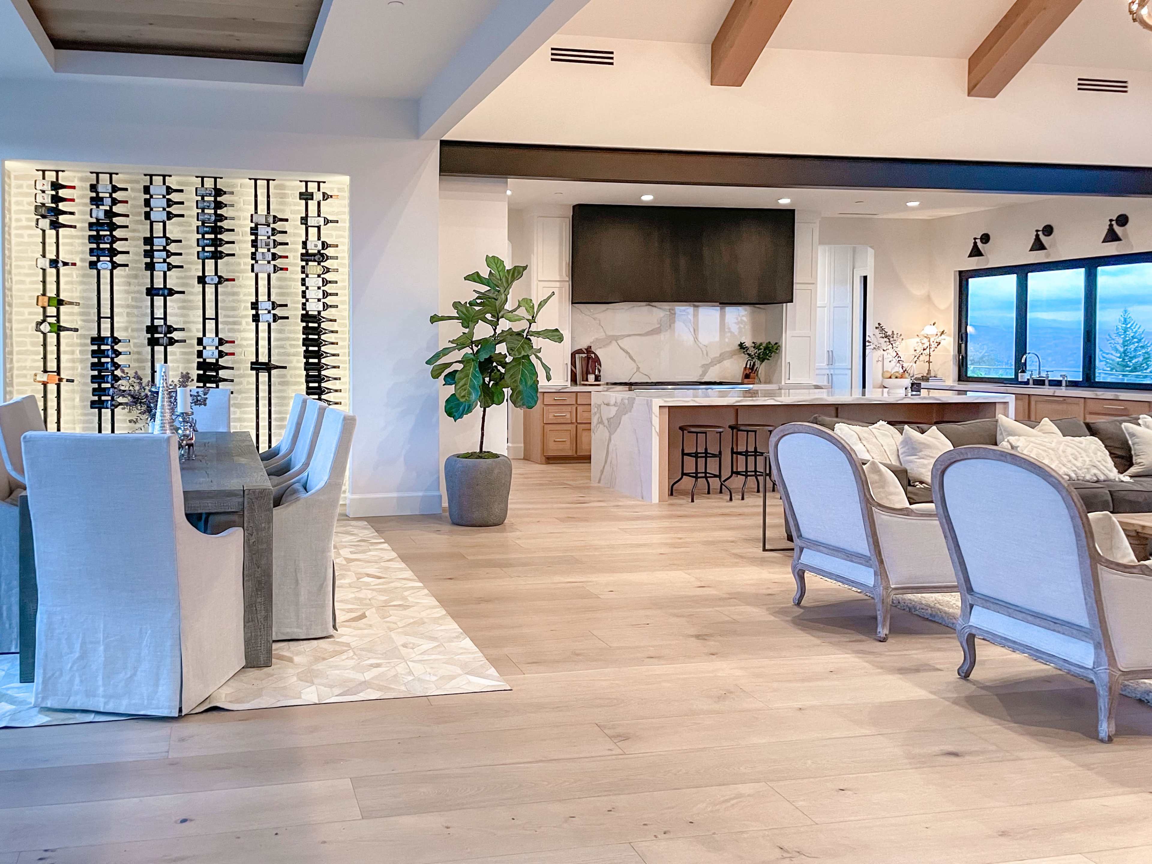 An open-concept living area featuring a dining table with chairs, a kitchen with a large island, and a display of wine bottles on the wall.