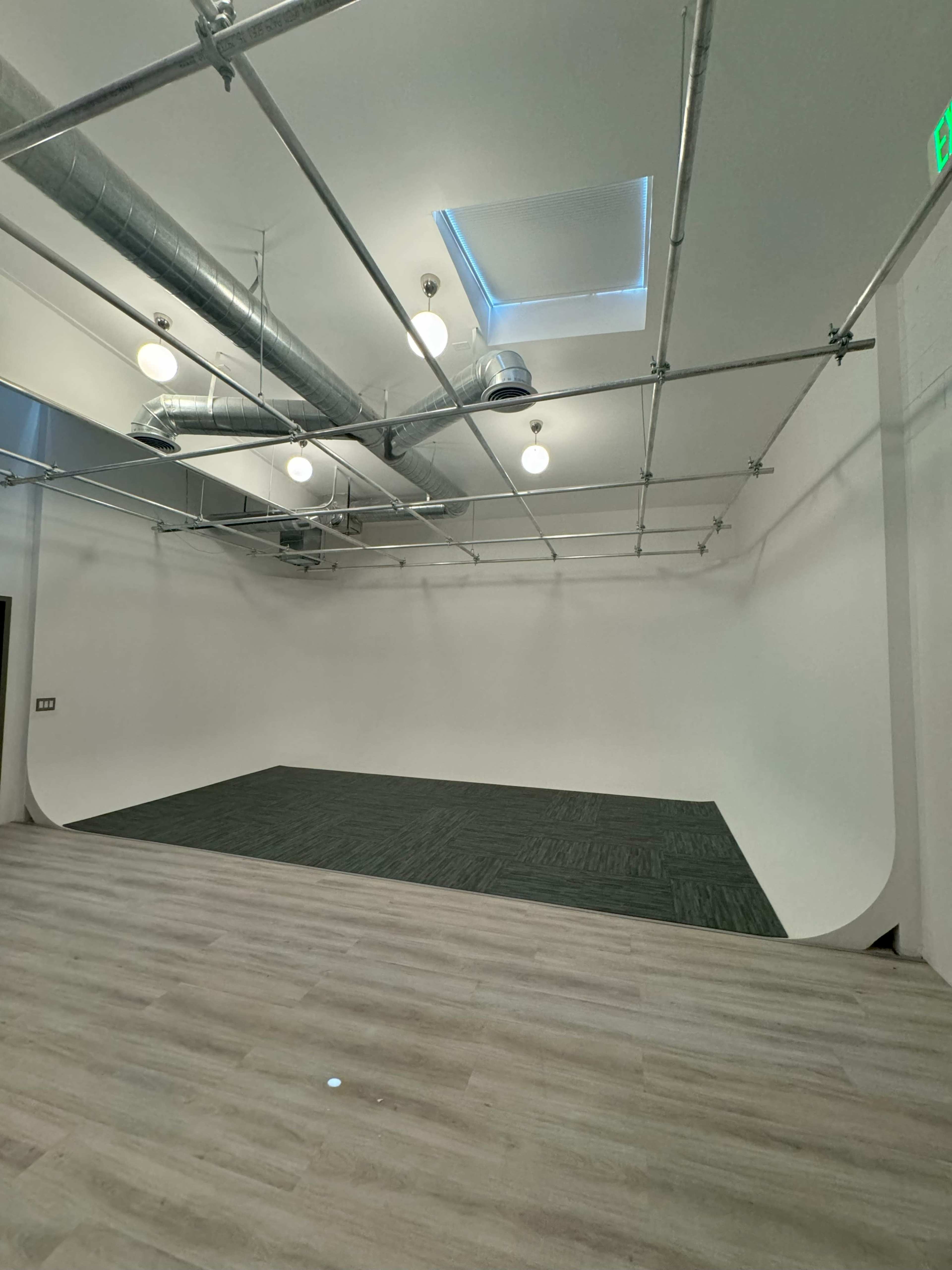An empty studio space with a seamless white backdrop, gray flooring, and overhead lighting fixtures.