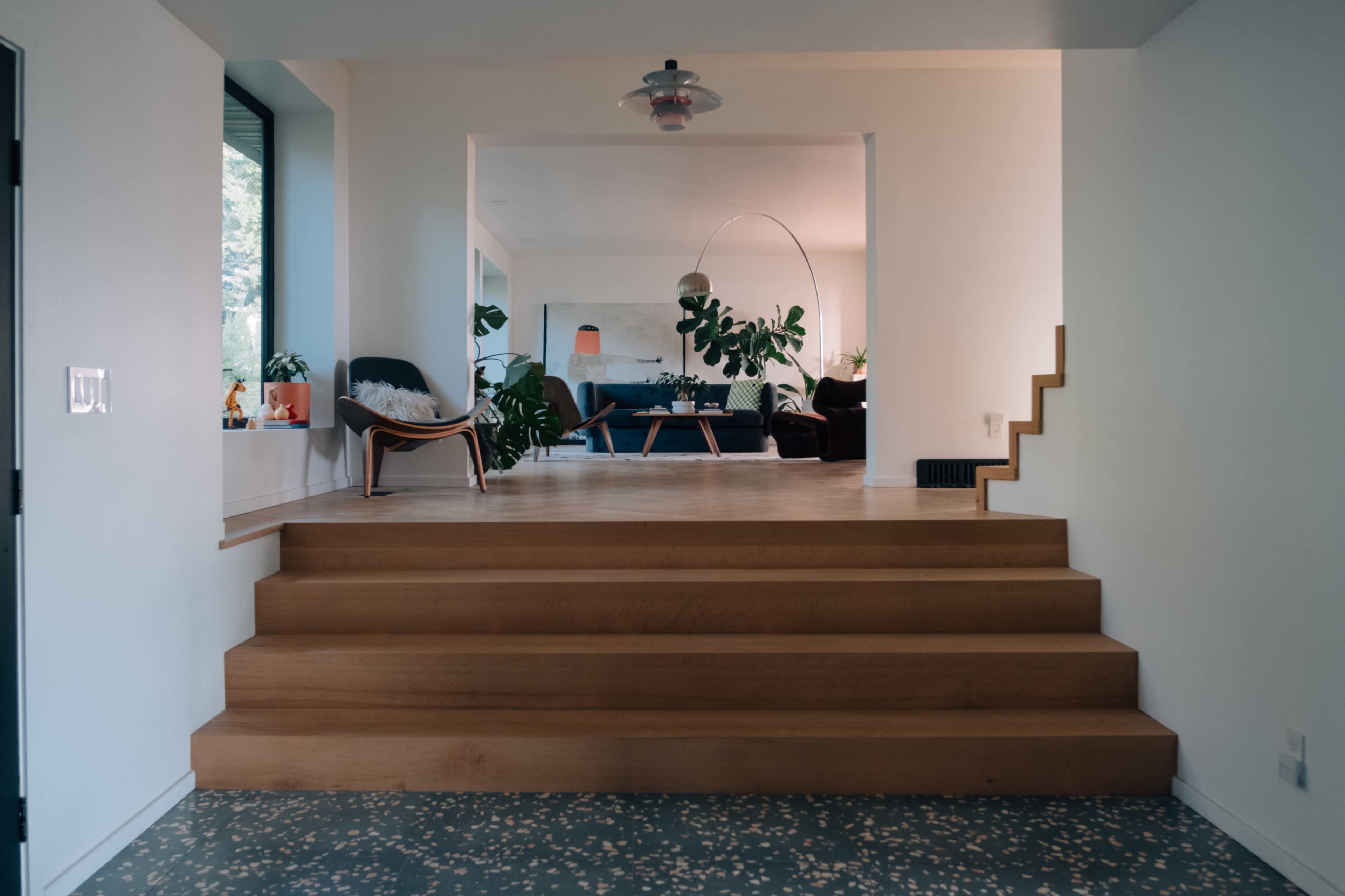 A spacious interior features a set of wooden stairs leading to a living area with seating and plants.