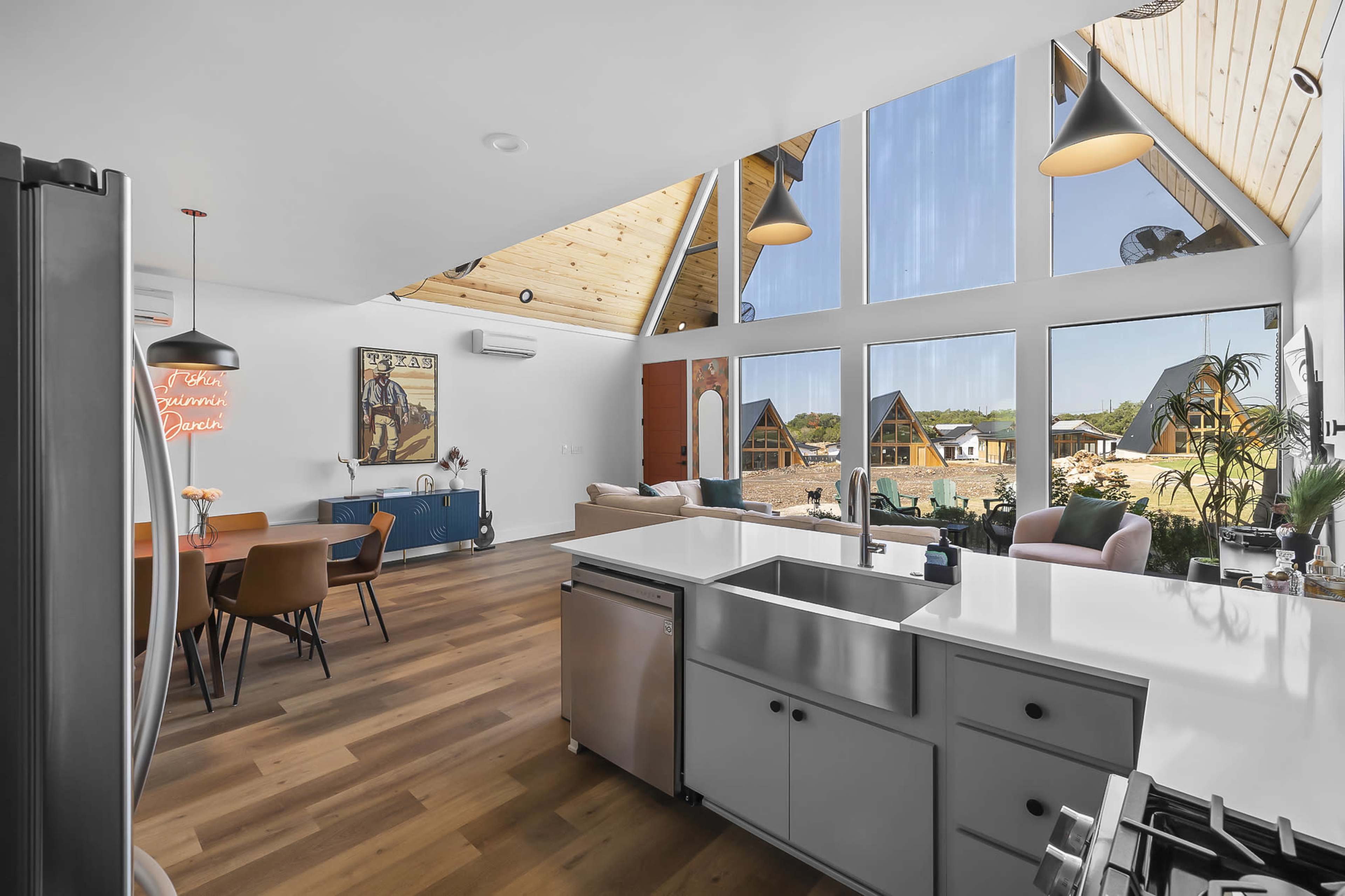 A modern kitchen and living area with large windows, wooden ceilings, and a dining space featuring a colorful artwork on the wall.