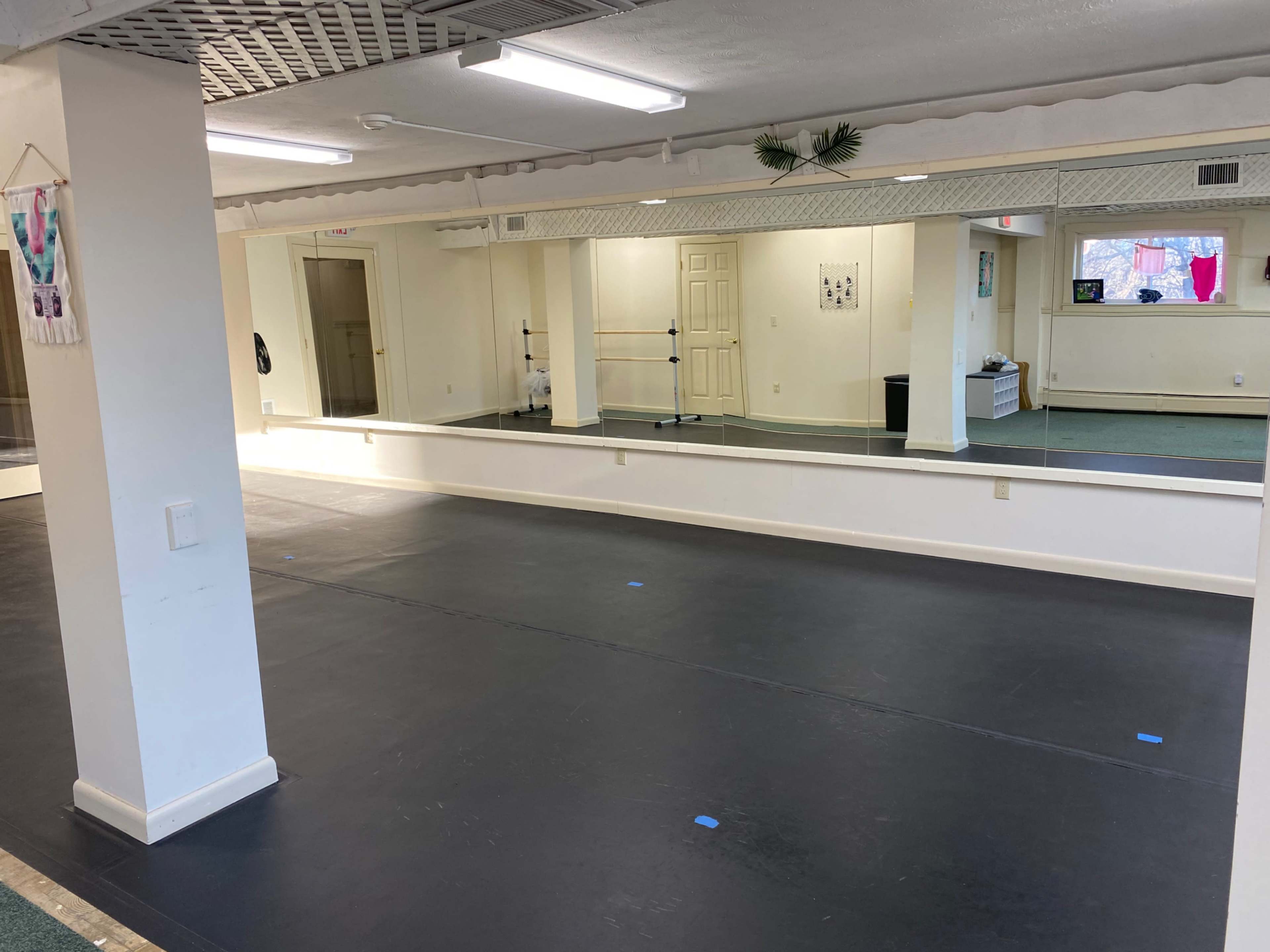 A spacious mirror-lined dance studio with a black floor and white walls.