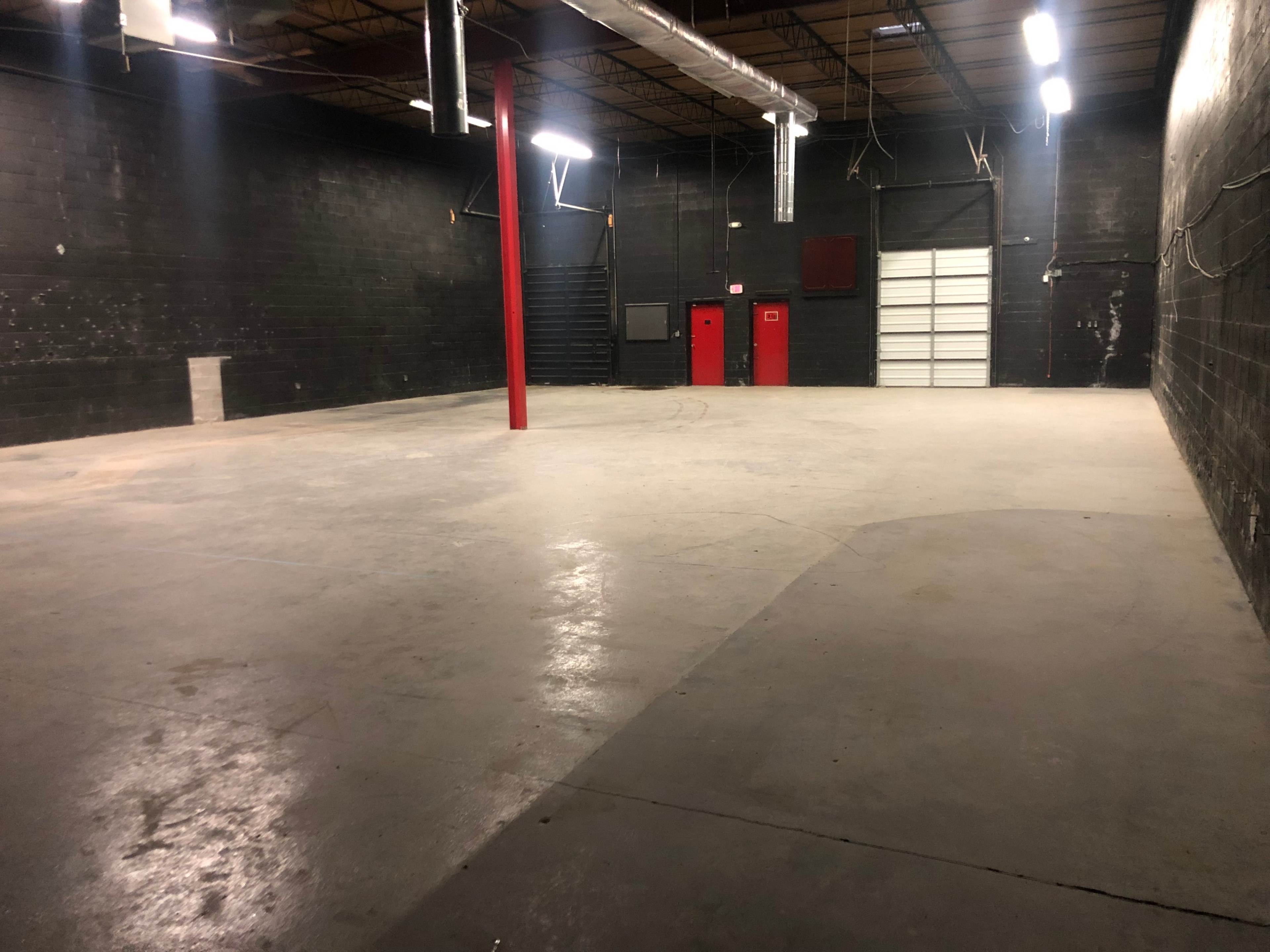 An empty industrial warehouse space with a concrete floor and black-painted walls.