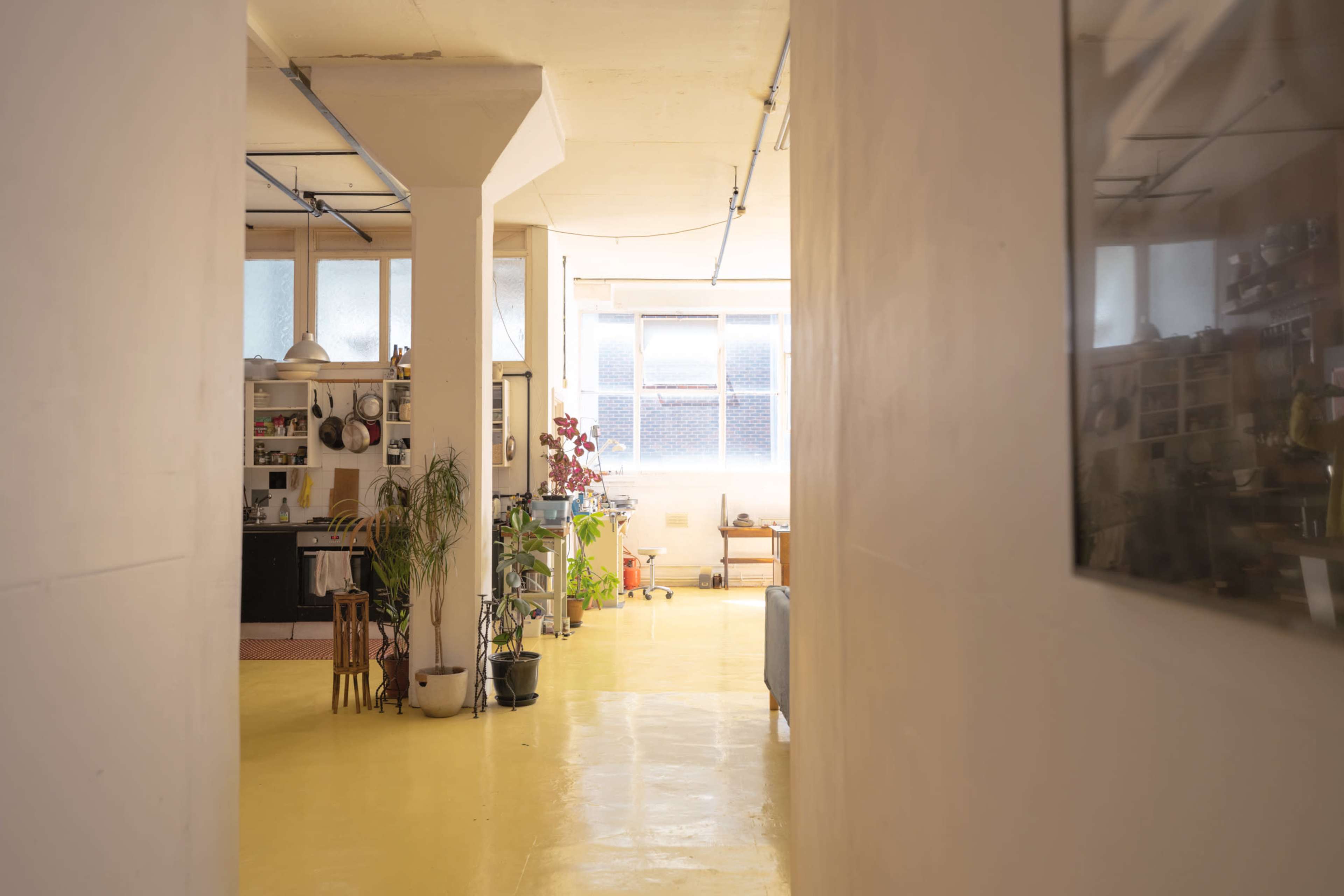 A hallway with yellow flooring leads to a bright room featuring a kitchen and a seating area.