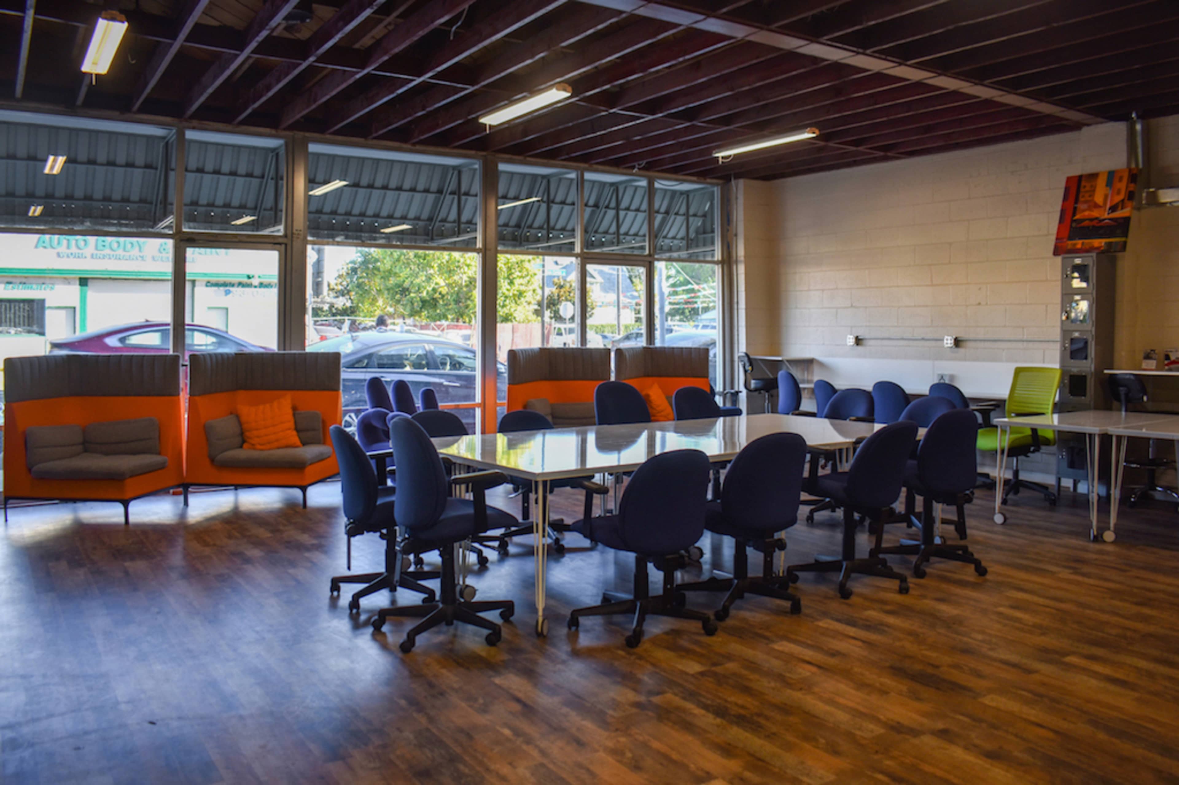 The image shows a spacious meeting room with a large table surrounded by blue chairs and orange seating areas along the windows.
