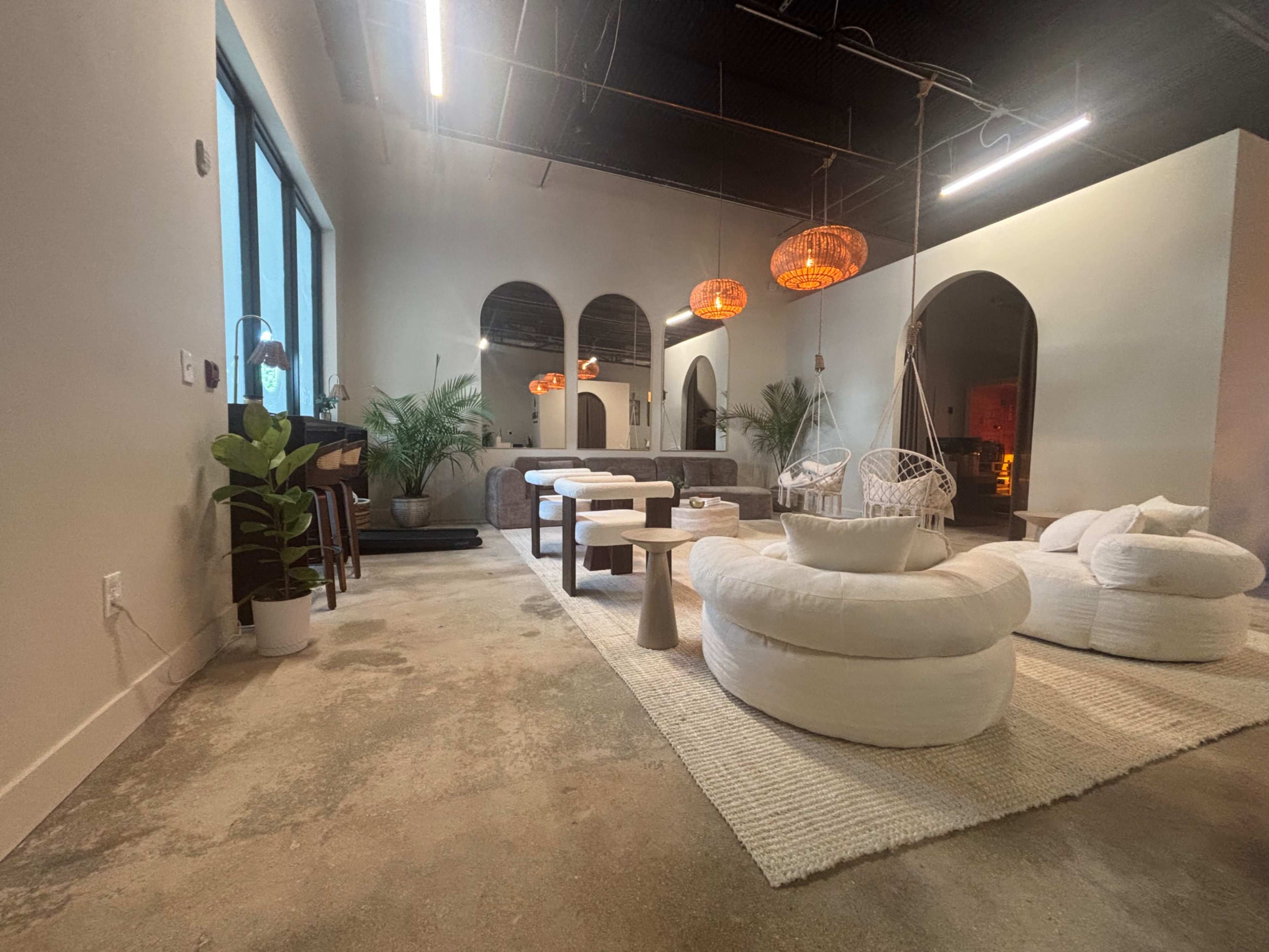The image shows a modern, minimalist lounge area featuring plush seating, a light-colored rug, and decorative hanging light fixtures.