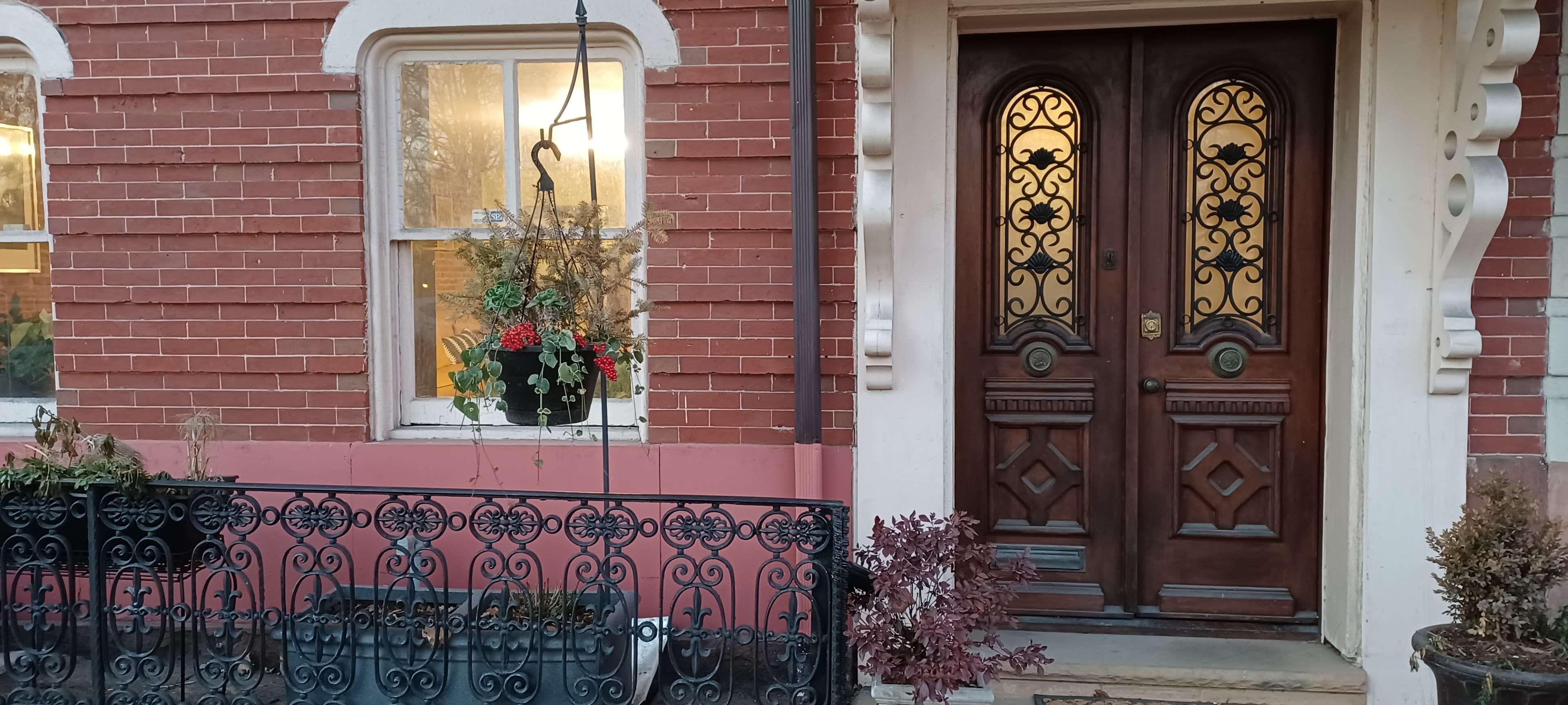 A brick townhouse with an ornate wooden door and a hanging planter by the window.