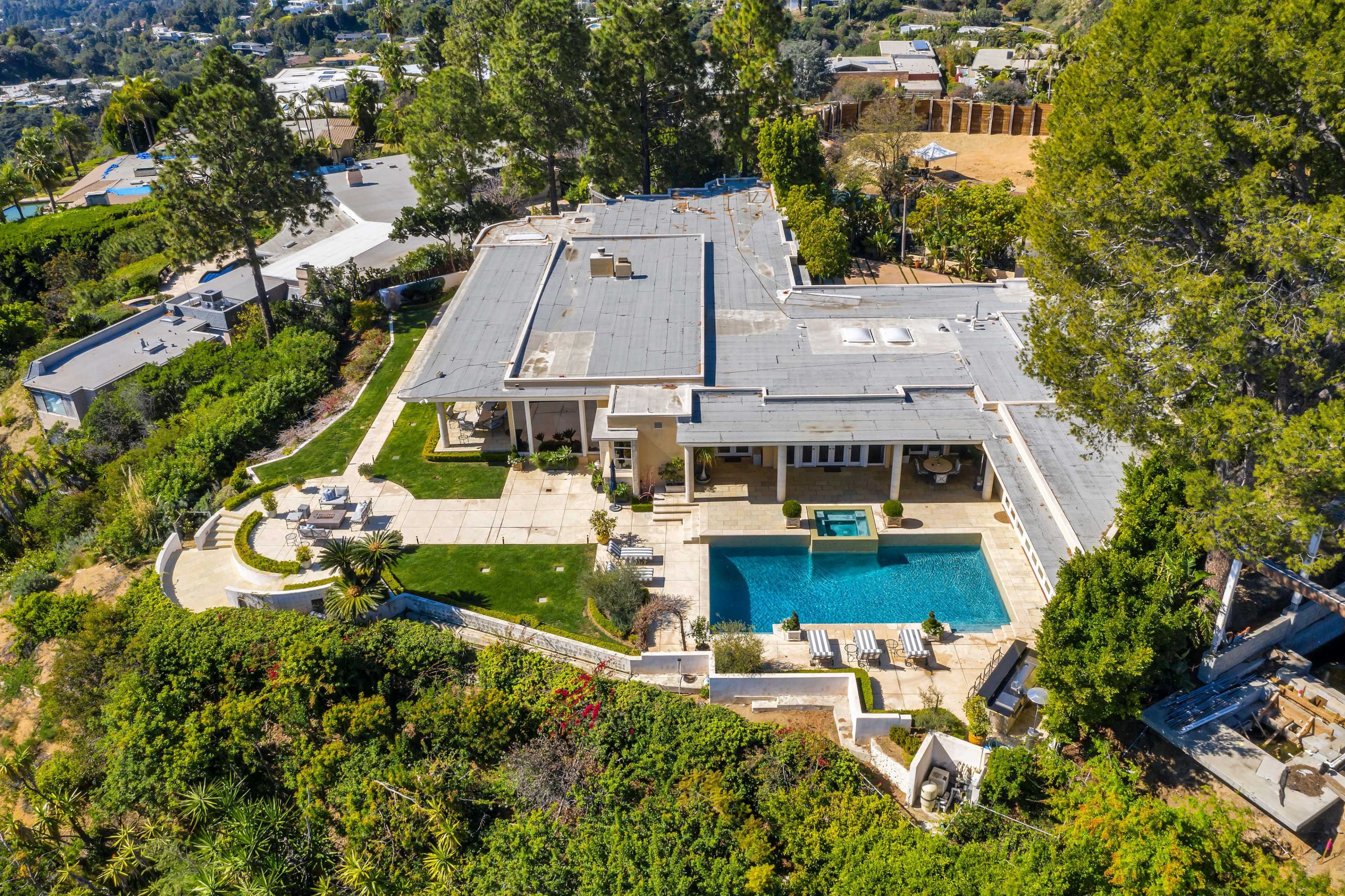 A modern house with a swimming pool and landscaped outdoor areas, situated amidst trees and greenery.