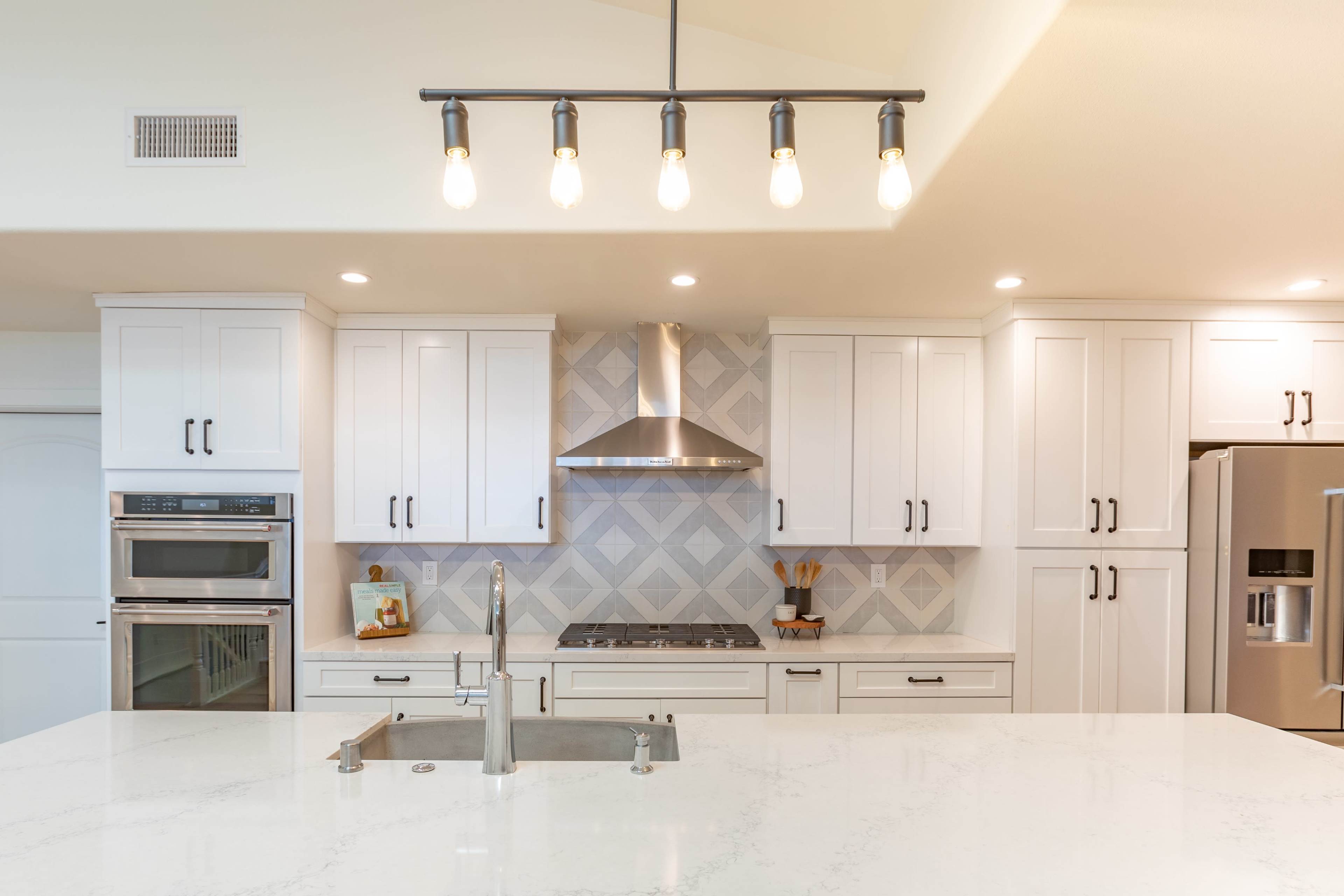 A modern kitchen features white cabinetry, a stainless steel oven and hood, and a large island with a sink.