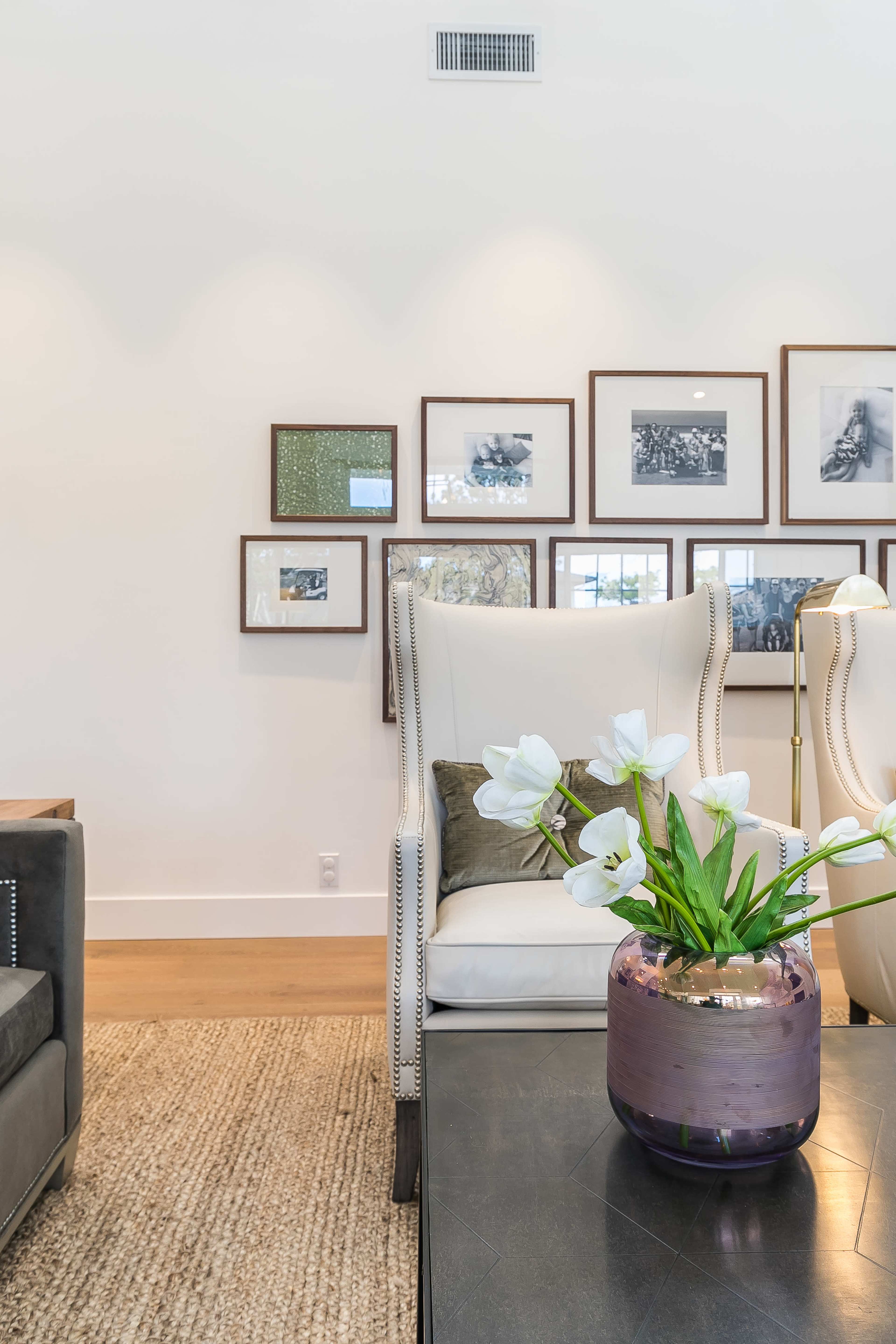A modern living room featuring a potted plant with white flowers on a dark coffee table, accompanied by a gallery wall of framed pictures in the background.
