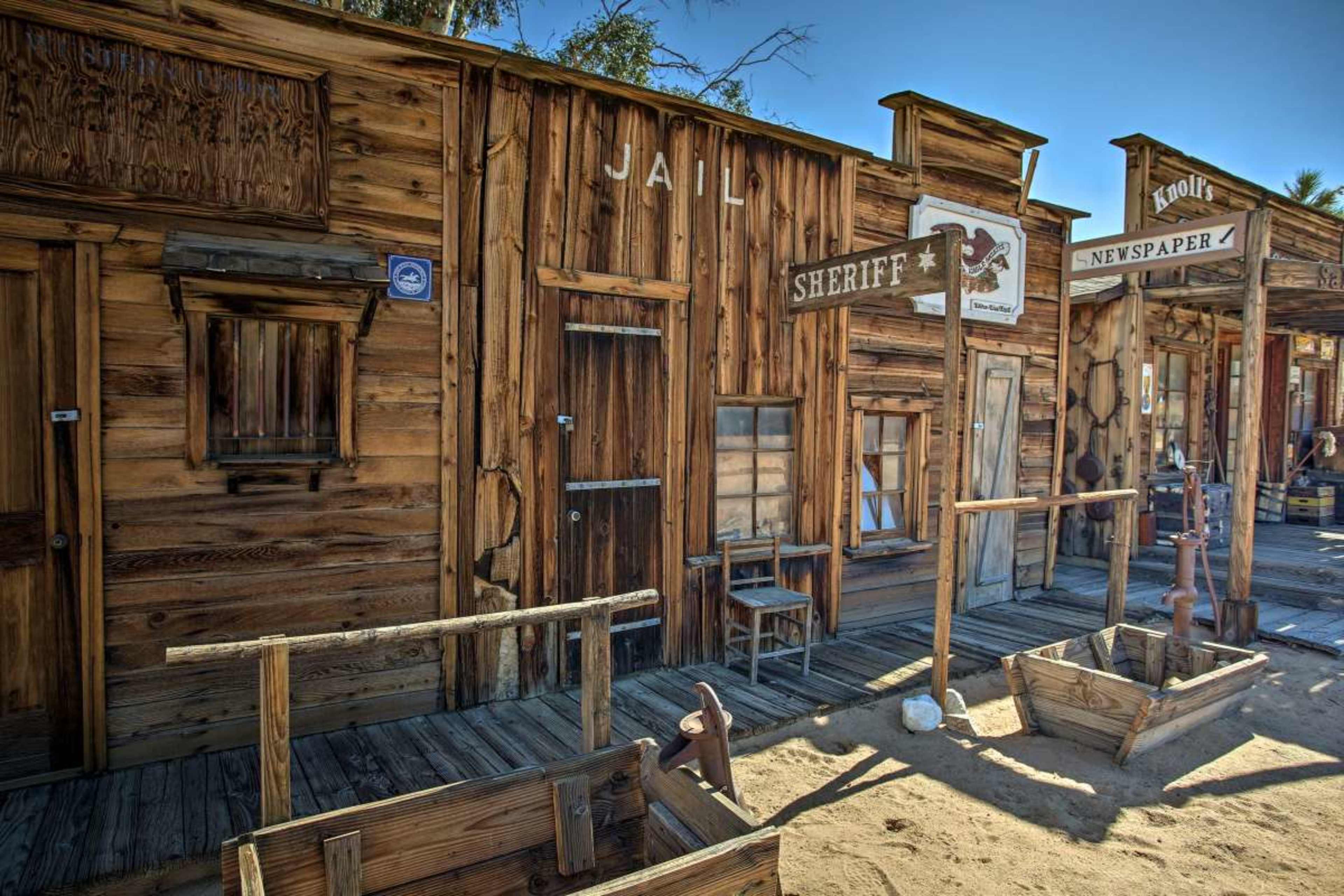 A western-style street with wooden buildings, including a jail and a sheriff's office, set against a clear blue sky.