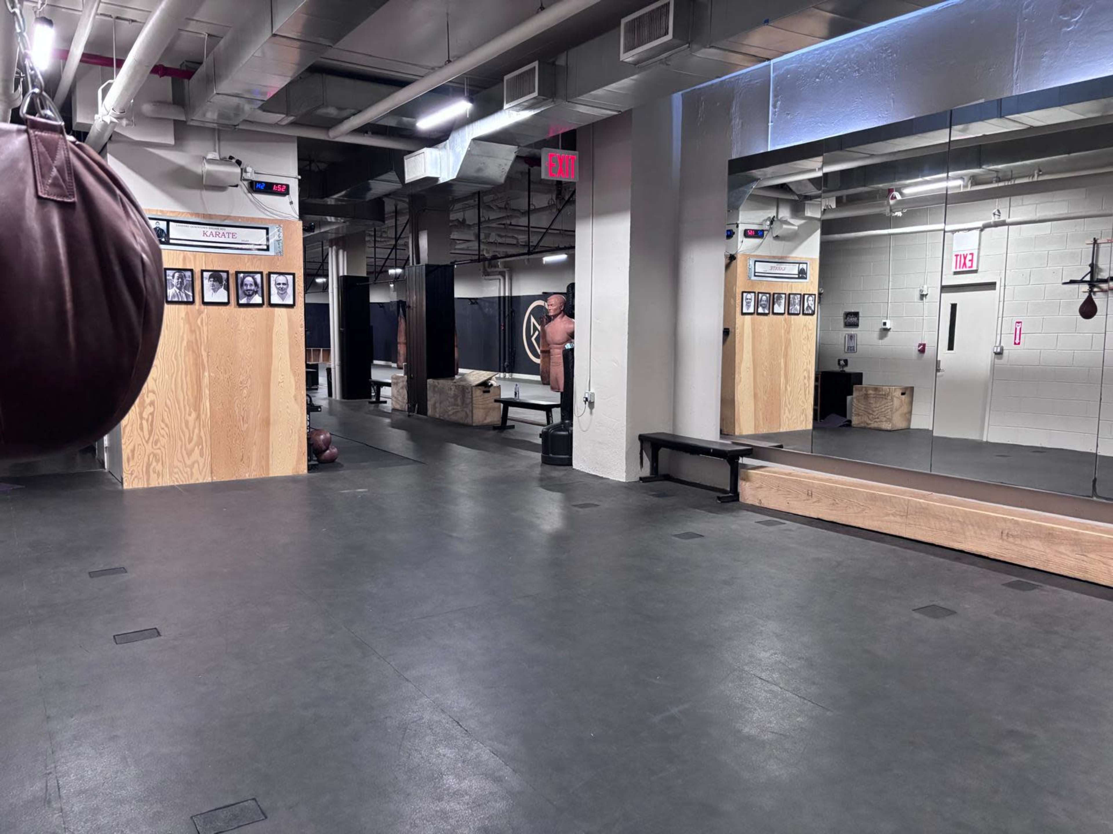 The image shows an empty boxing gym featuring mirrored walls, a hanging punching bag, and wooden boxes along the perimeter.