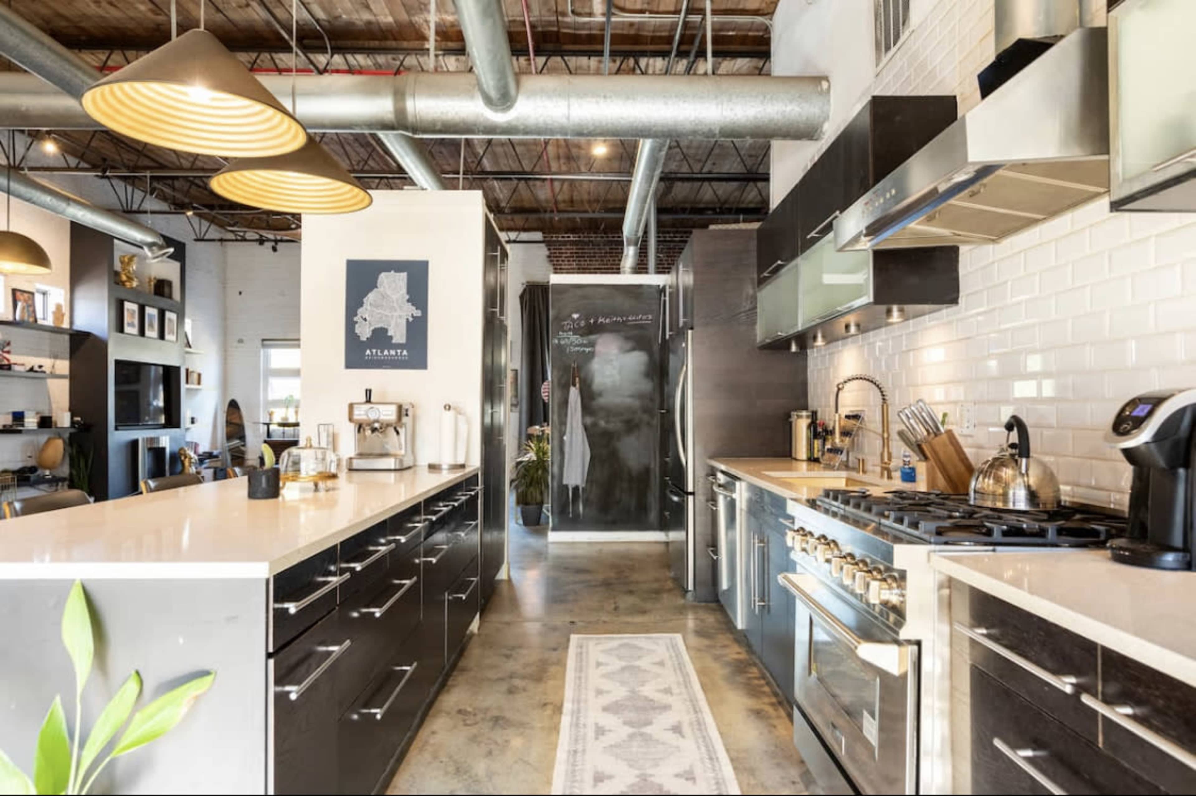 A modern kitchen with sleek black cabinetry, stainless steel appliances, and a central island, leading to an open living space.
