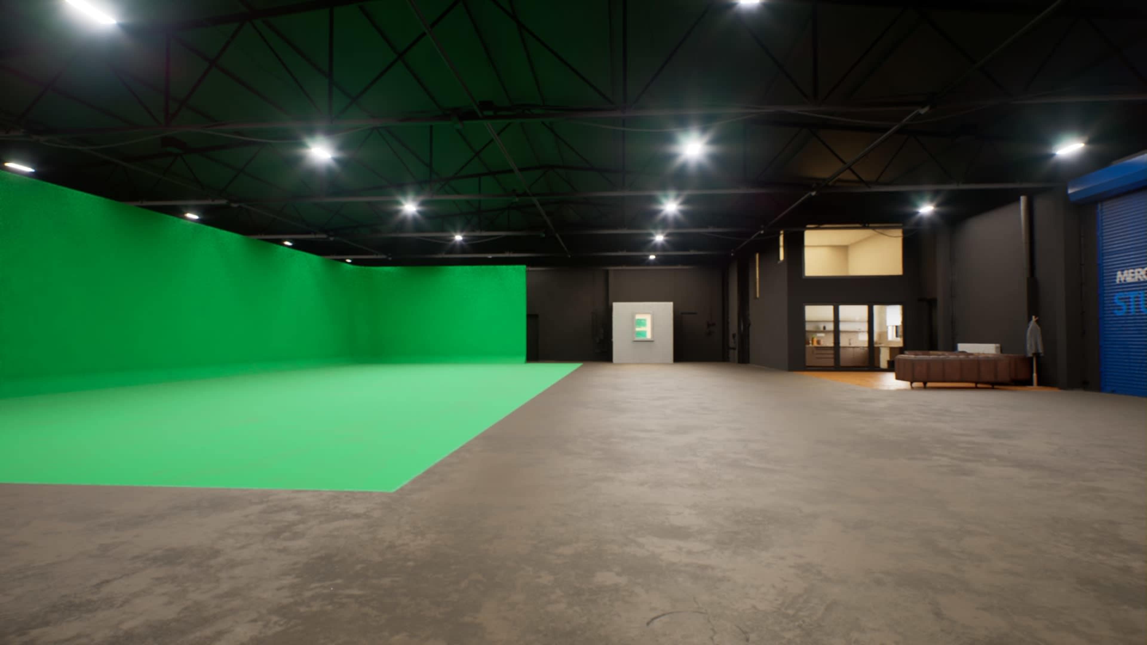 A spacious warehouse interior featuring a large green screen on one side and an entrance to a room on the right, with industrial lighting overhead and a concrete floor.