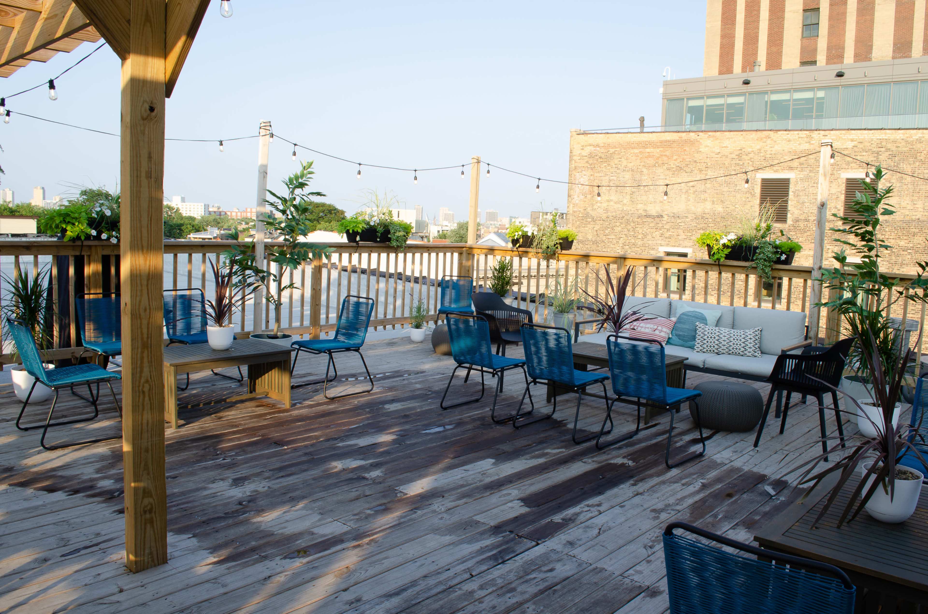 A rooftop deck with wooden flooring, various seating arrangements, potted plants, and string lights above.