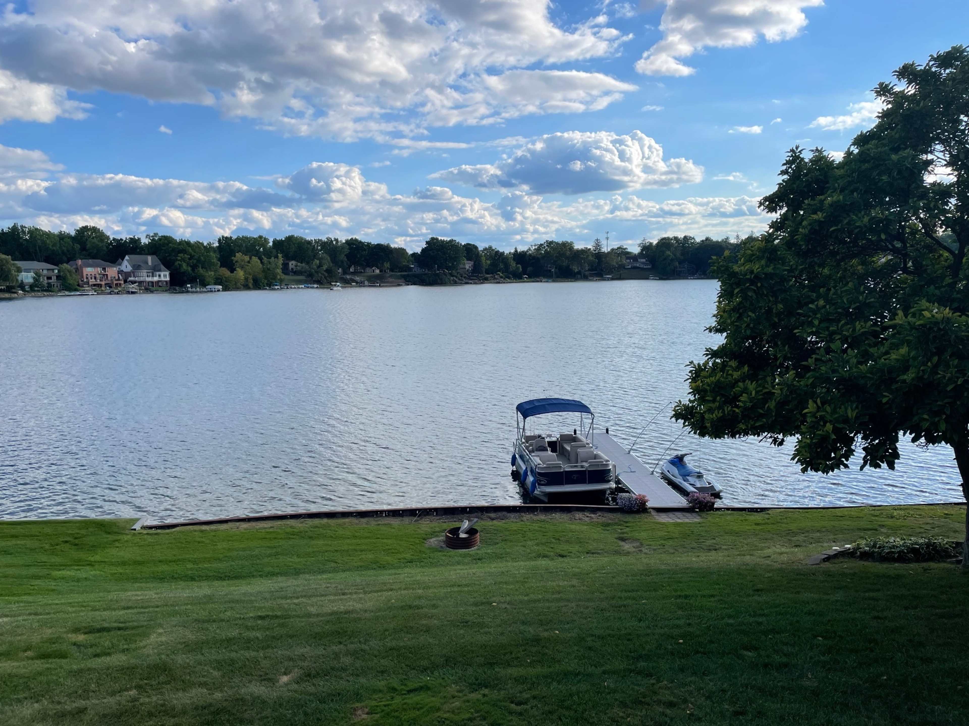 A boat is docked on a calm lake surrounded by grassy land and trees under a sky with scattered clouds.