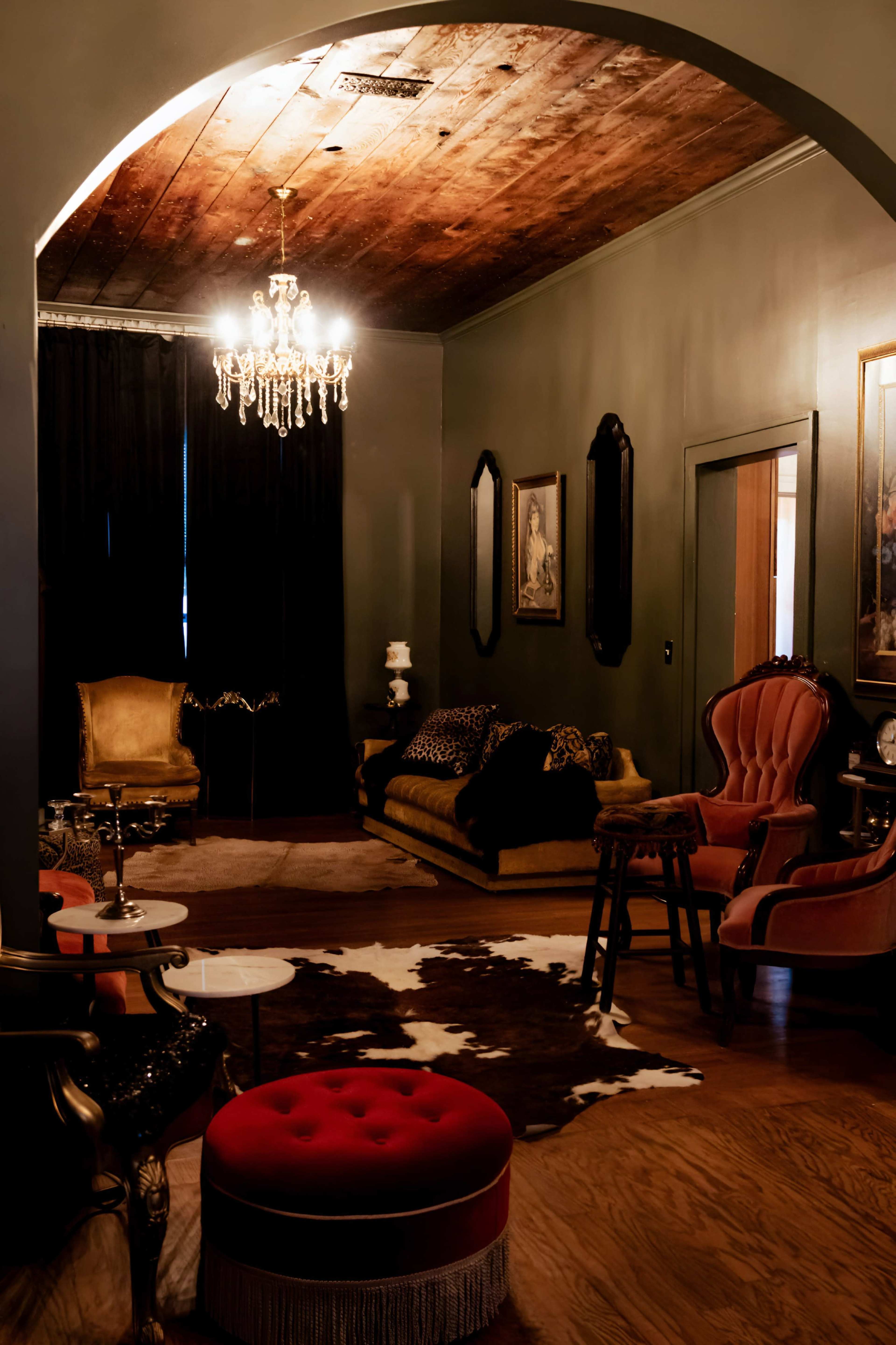 The image shows a dimly lit room featuring a chandelier, ornate furniture, and a cowhide rug on the wooden floor.