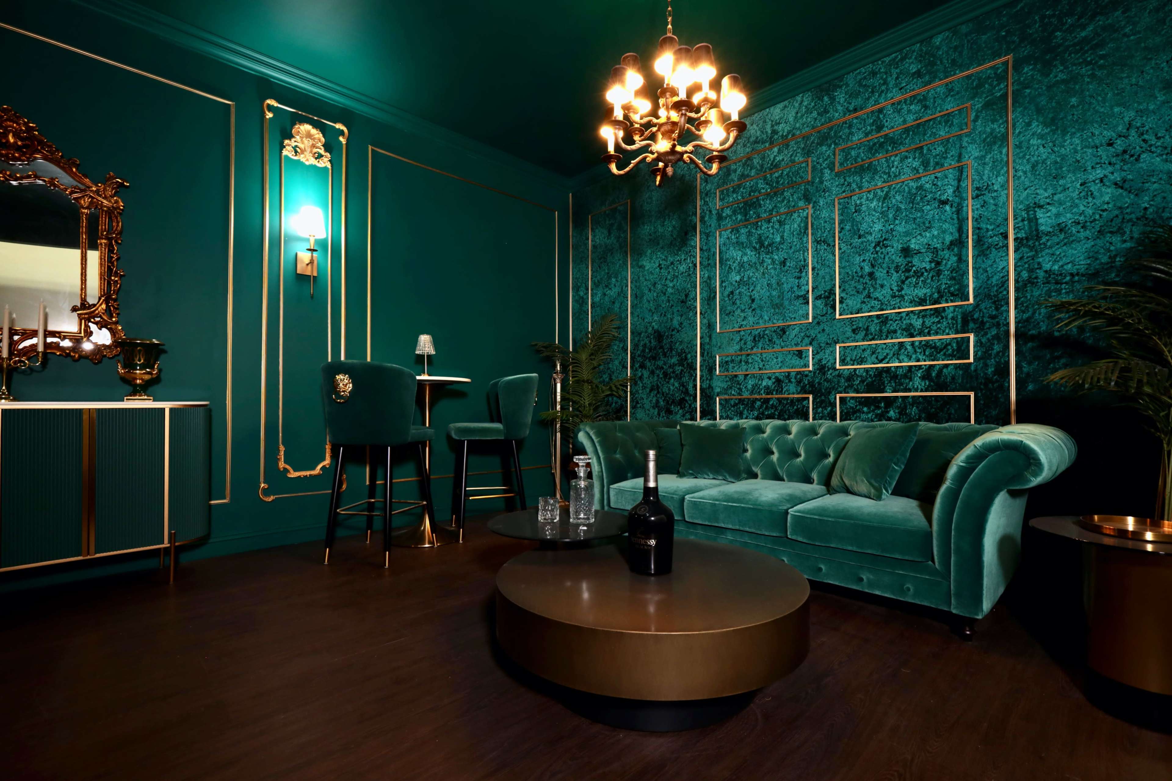 An elegant room with teal walls, a plush velvet sofa, a round coffee table, and a chandelier.