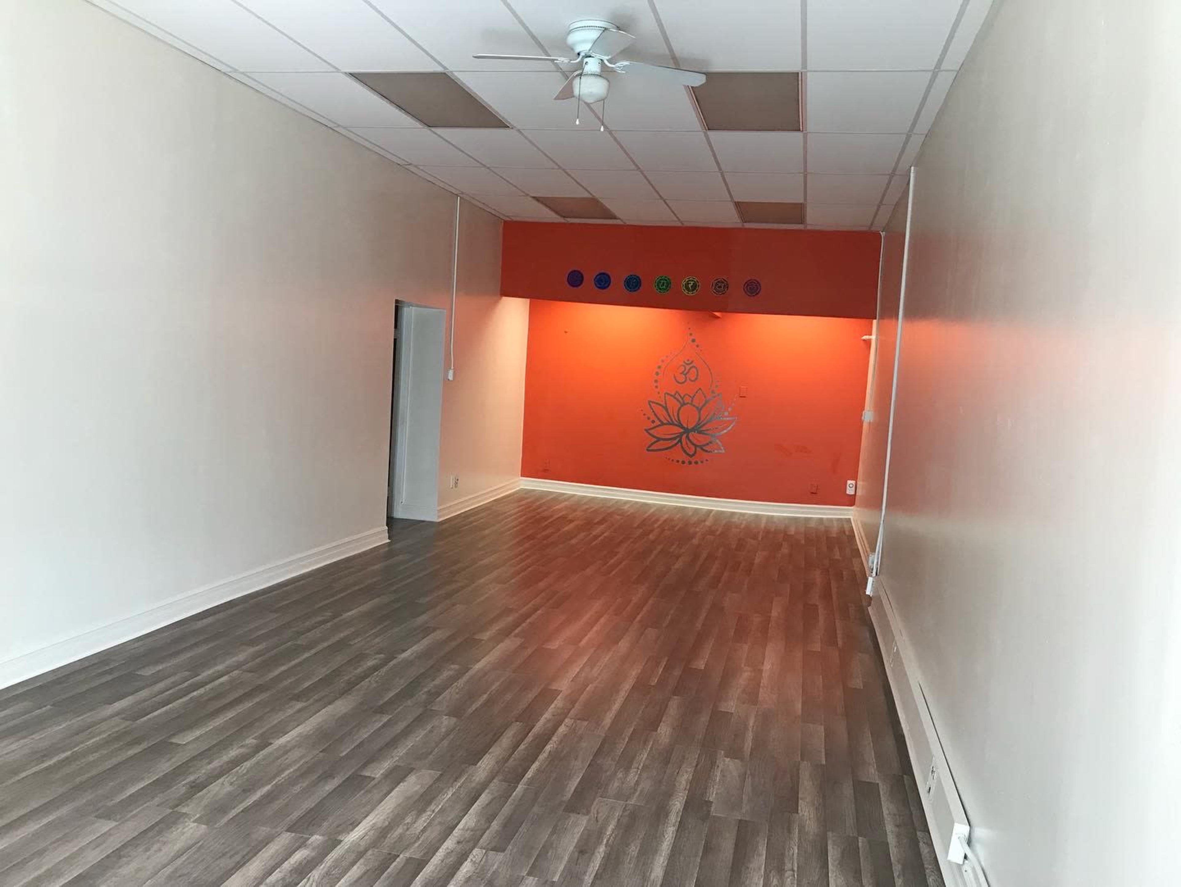 A spacious room with light-colored walls, a lotus flower mural on an orange accent wall, and a wooden floor.