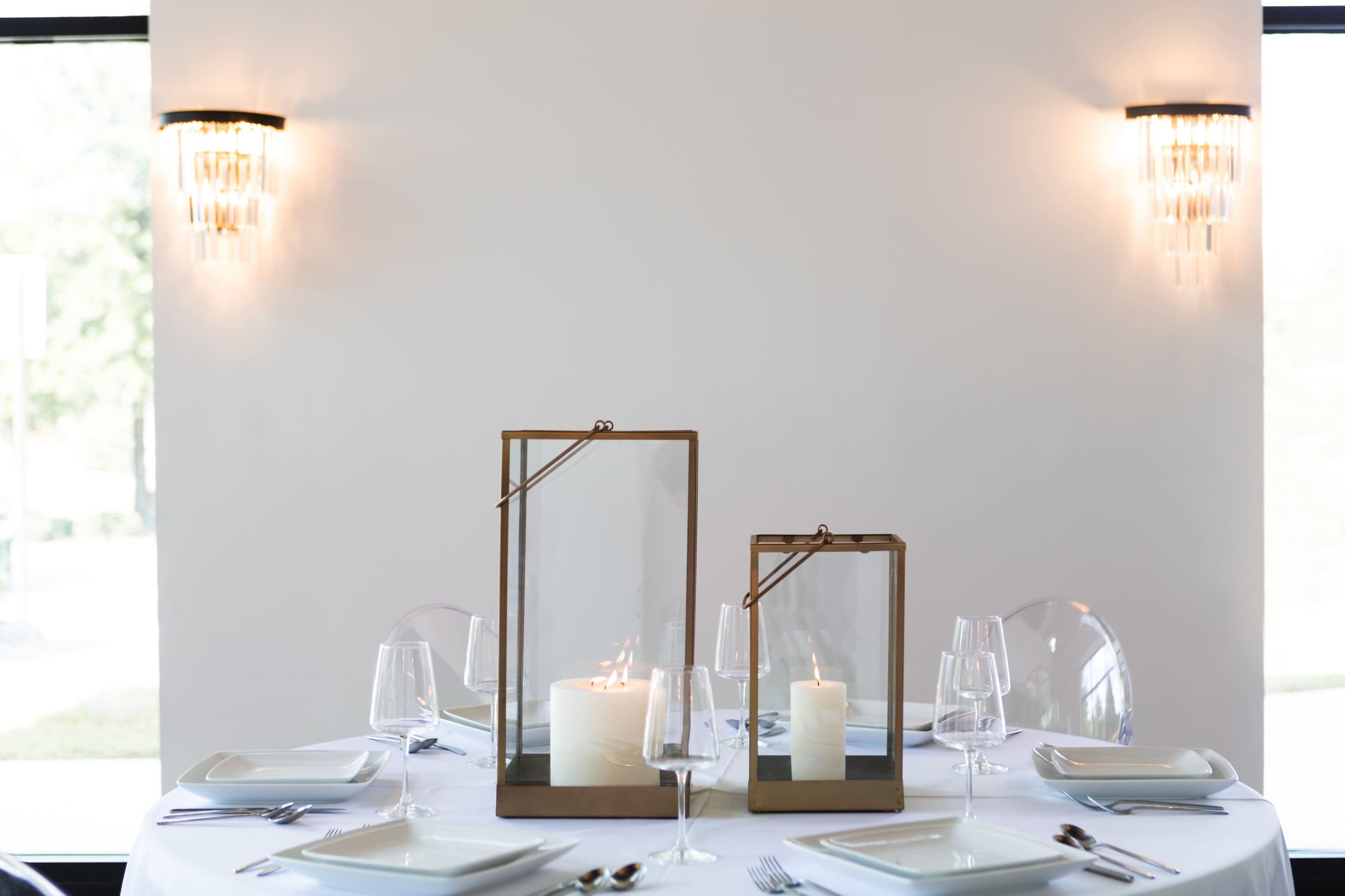 A elegantly set dining table with two glass candle holders and multiple place settings.