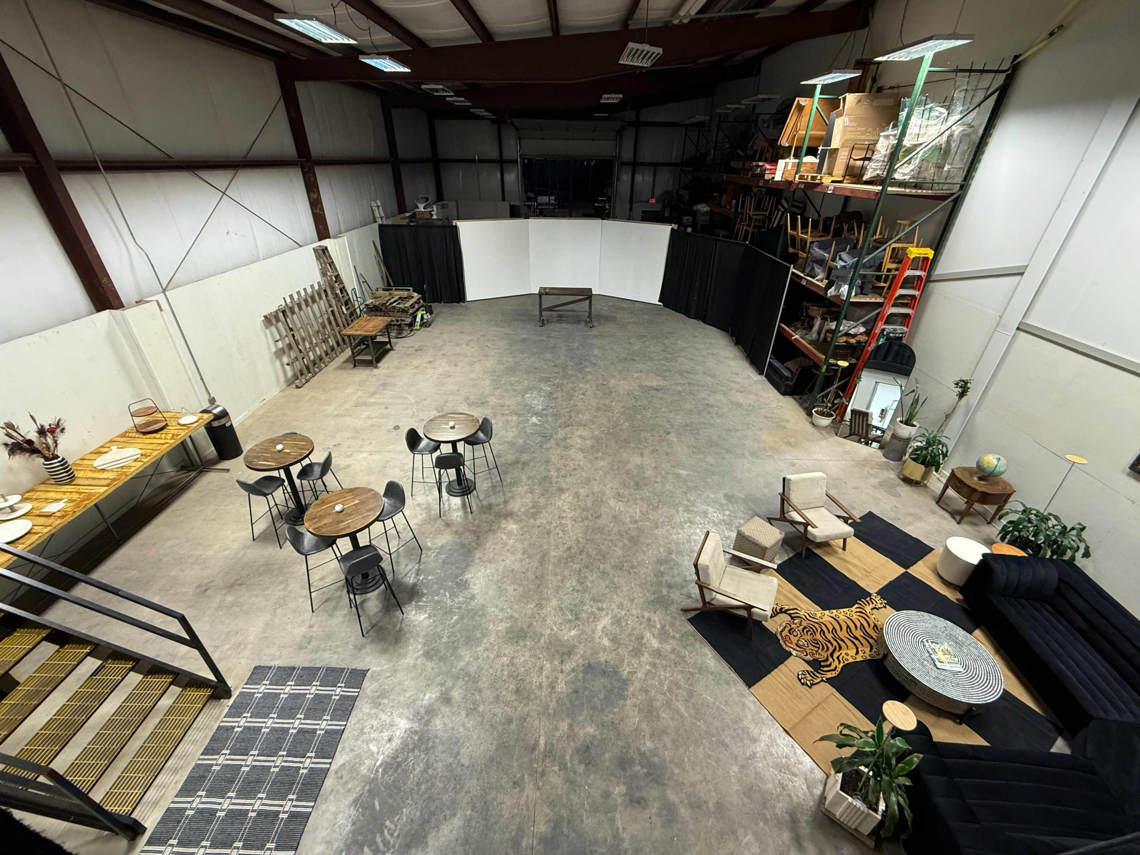 The image shows a spacious, industrial-style interior with seating, tables, and decorative elements arranged for an event or gathering.