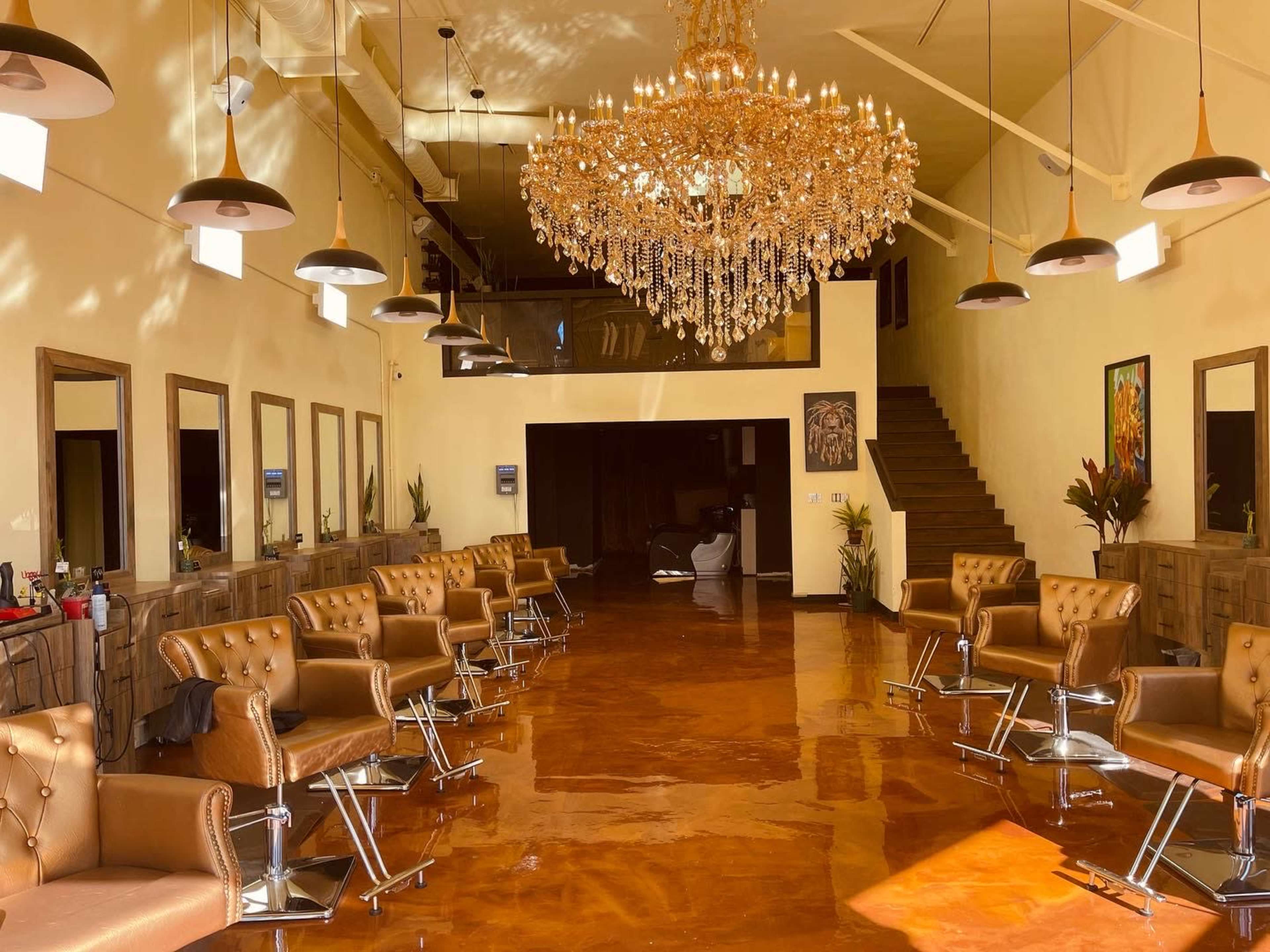 A spacious salon with brown leather chairs, a large chandelier, and a staircase in the background.