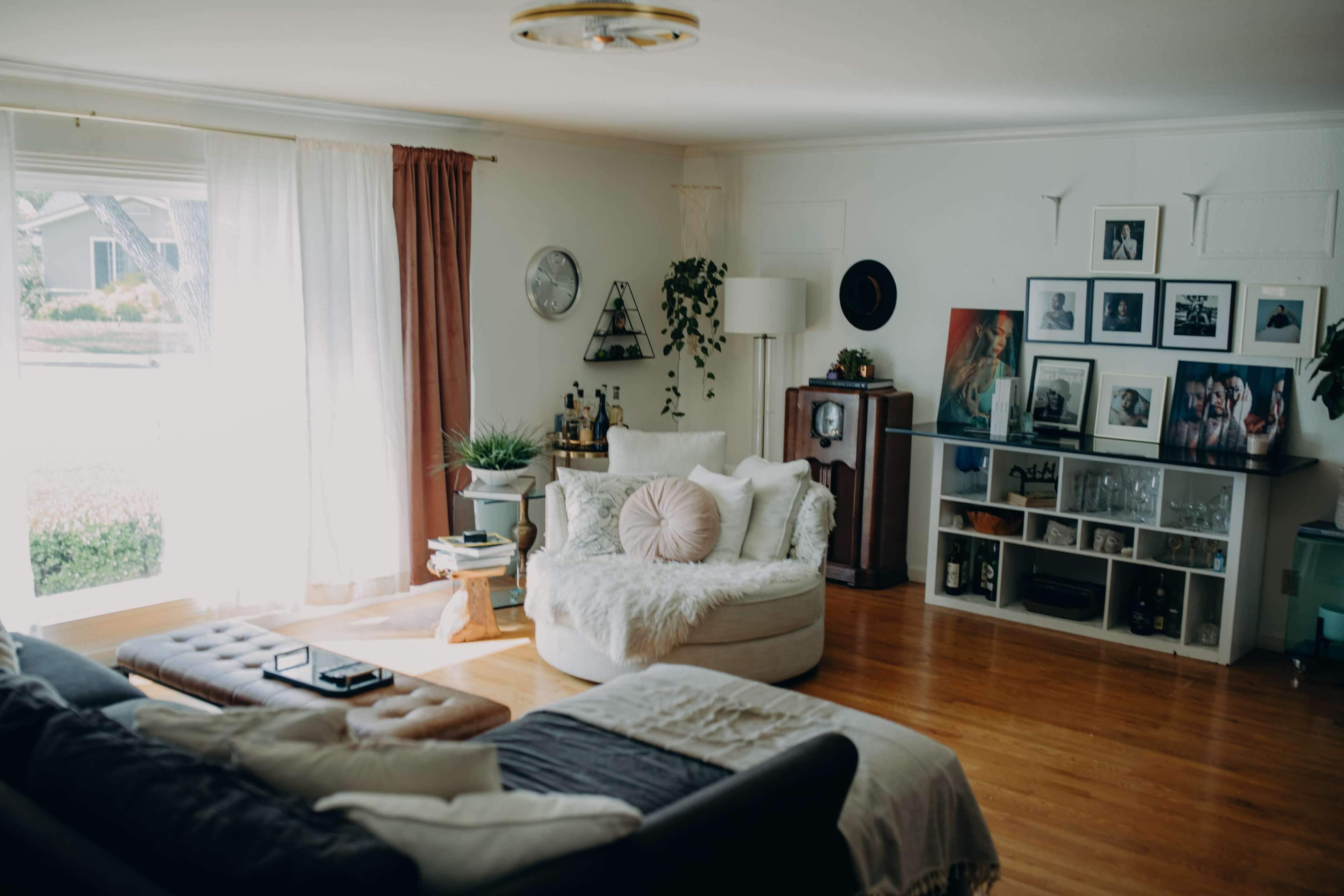 The living room features a cozy seating area with a large circular chair, a dark sofa, and various plants, along with a mix of framed artwork on the walls.