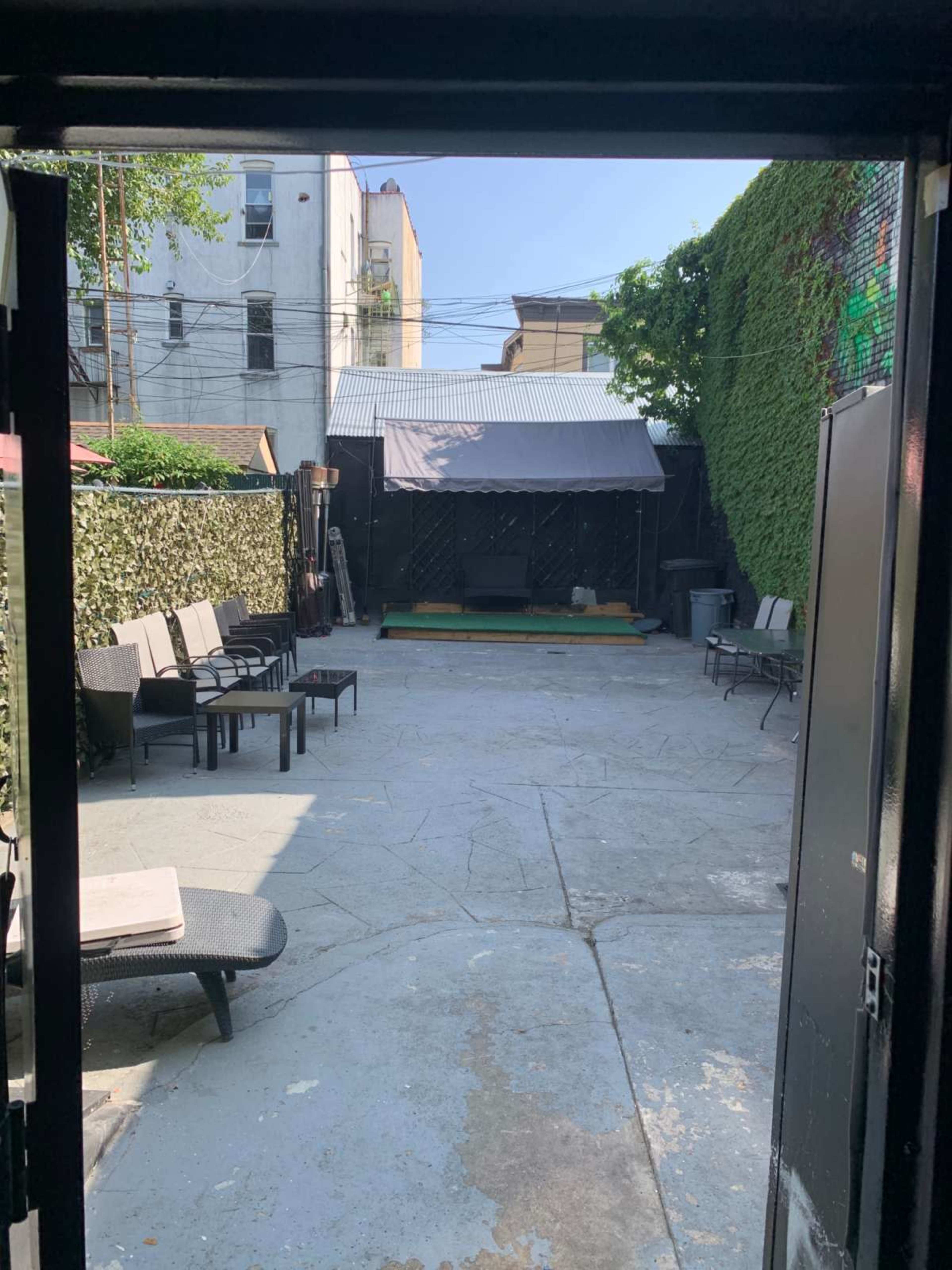 A small outdoor area is visible through a doorway, featuring several chairs arranged around a green stage and surrounded by greenery.
