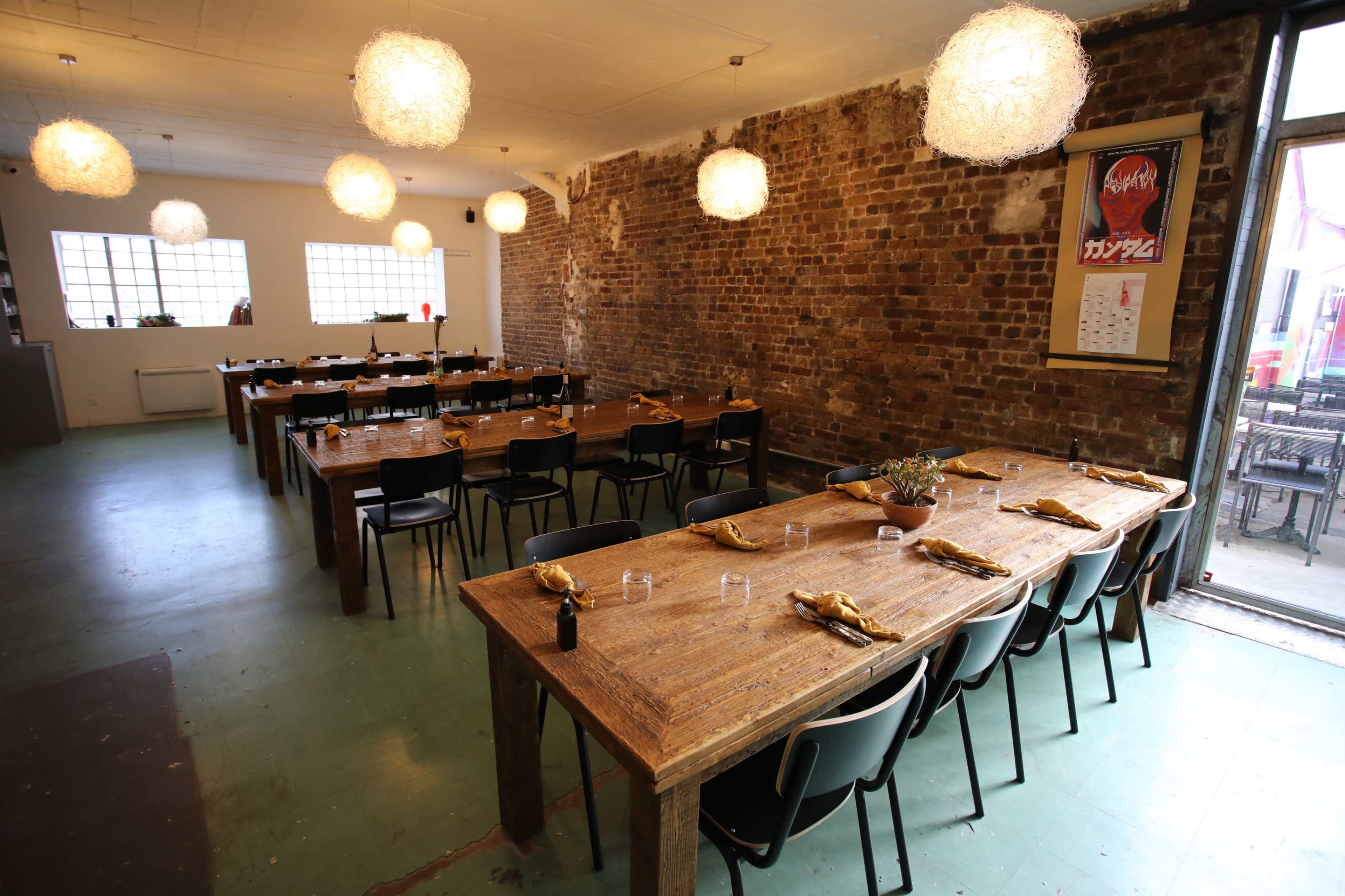 A spacious restaurant with wooden tables set for dining, exposed brick walls, and pendant lighting.