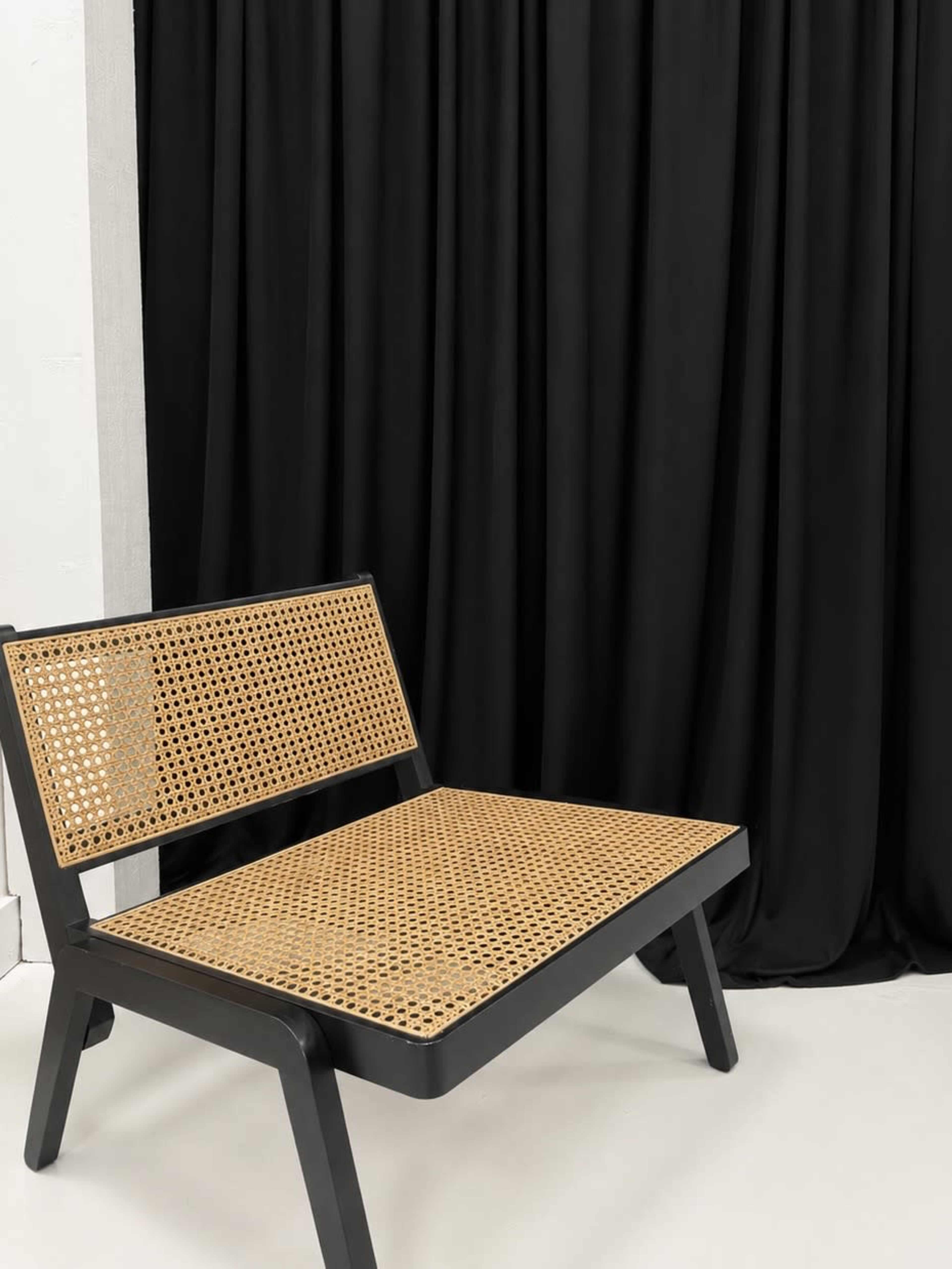 A wooden chair with a caned seat stands next to a black curtain.