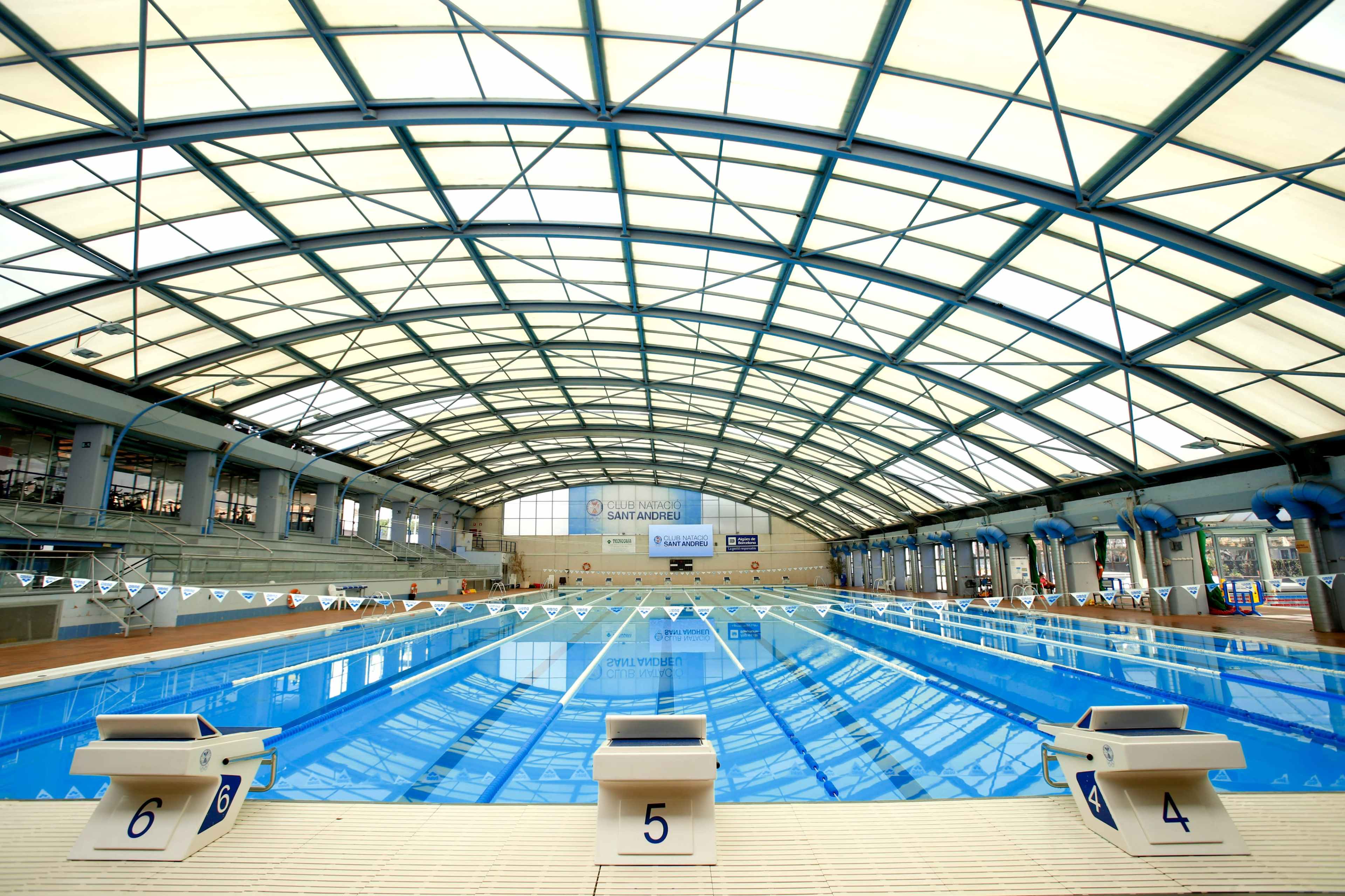 An indoor swimming pool with lanes marked by numbered starting blocks and a large arched roof.