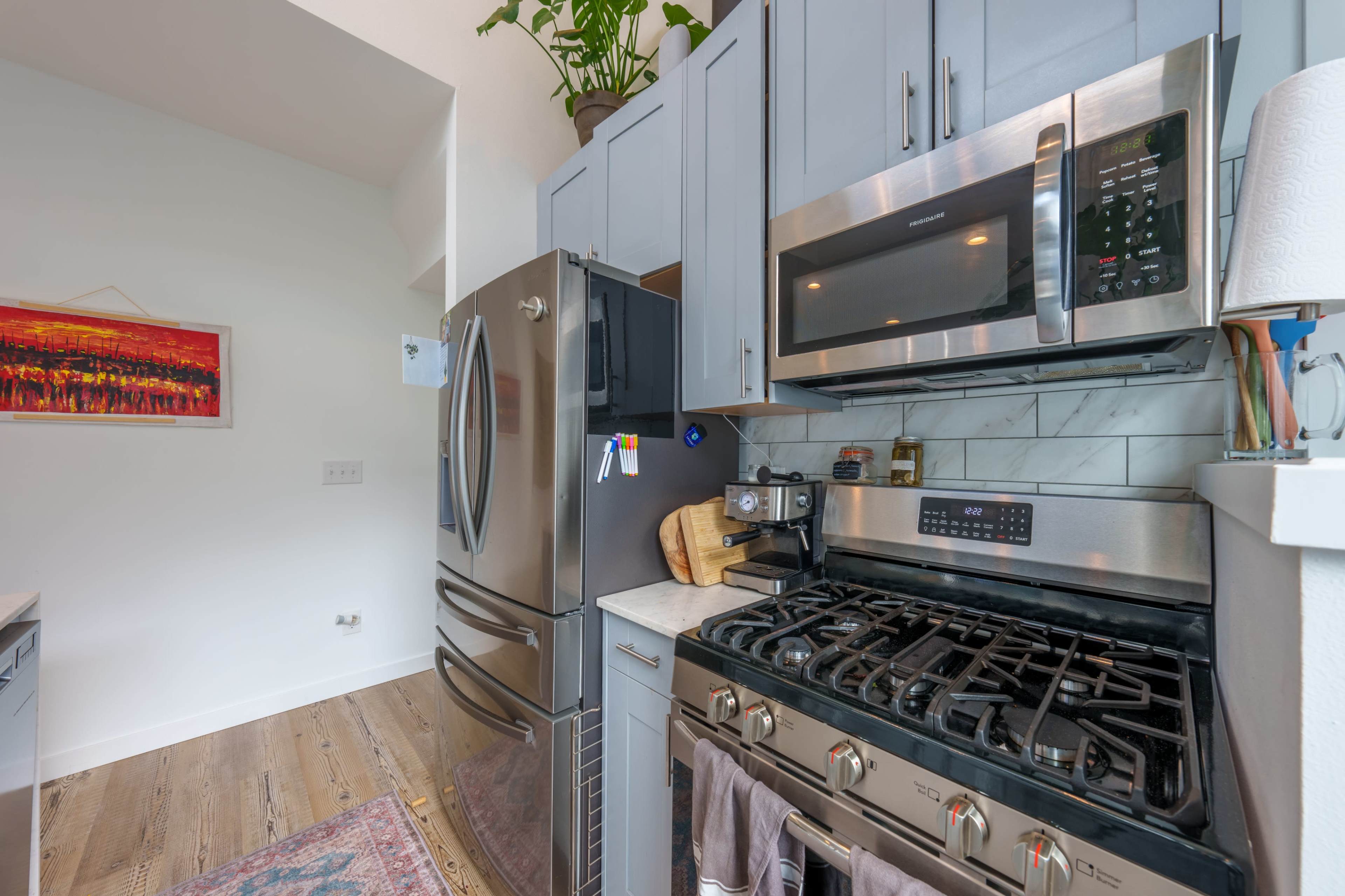 A modern kitchen features stainless steel appliances, light blue cabinets, and a window with a potted plant.