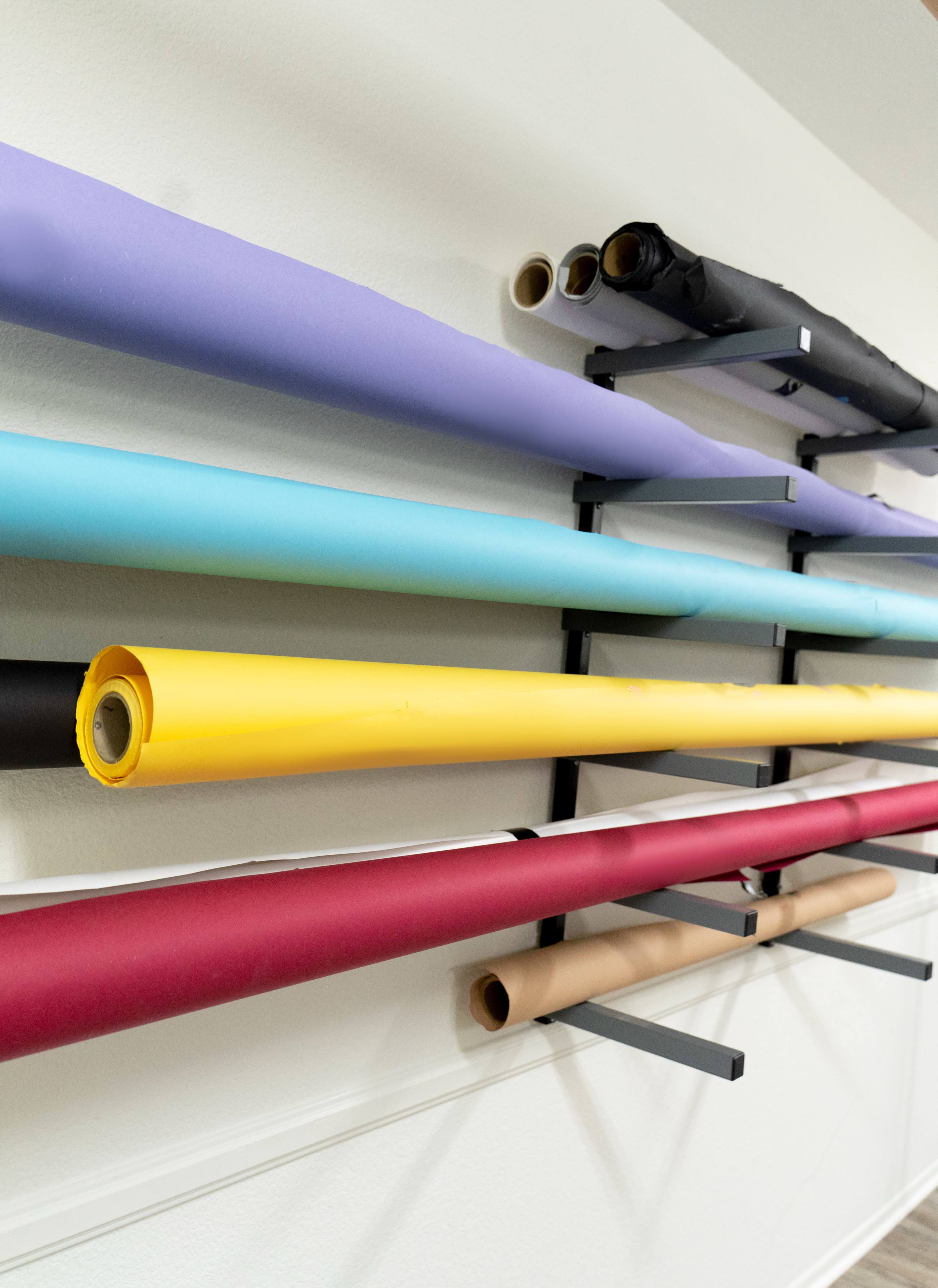 Rolls of colored paper are neatly organized on a wall-mounted rack.