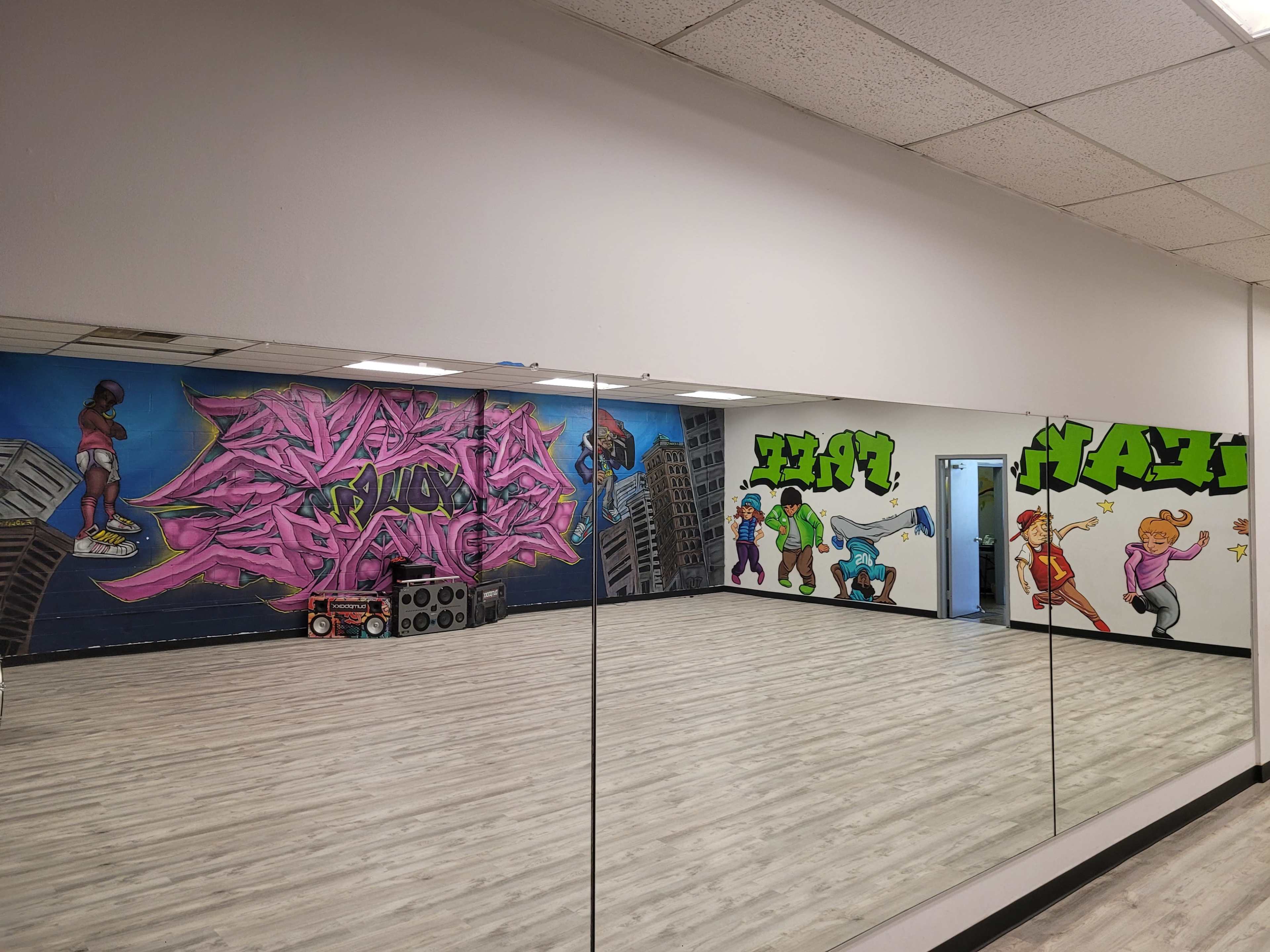 A dance studio with a large mirror, featuring colorful graffiti murals on the walls and wooden flooring.